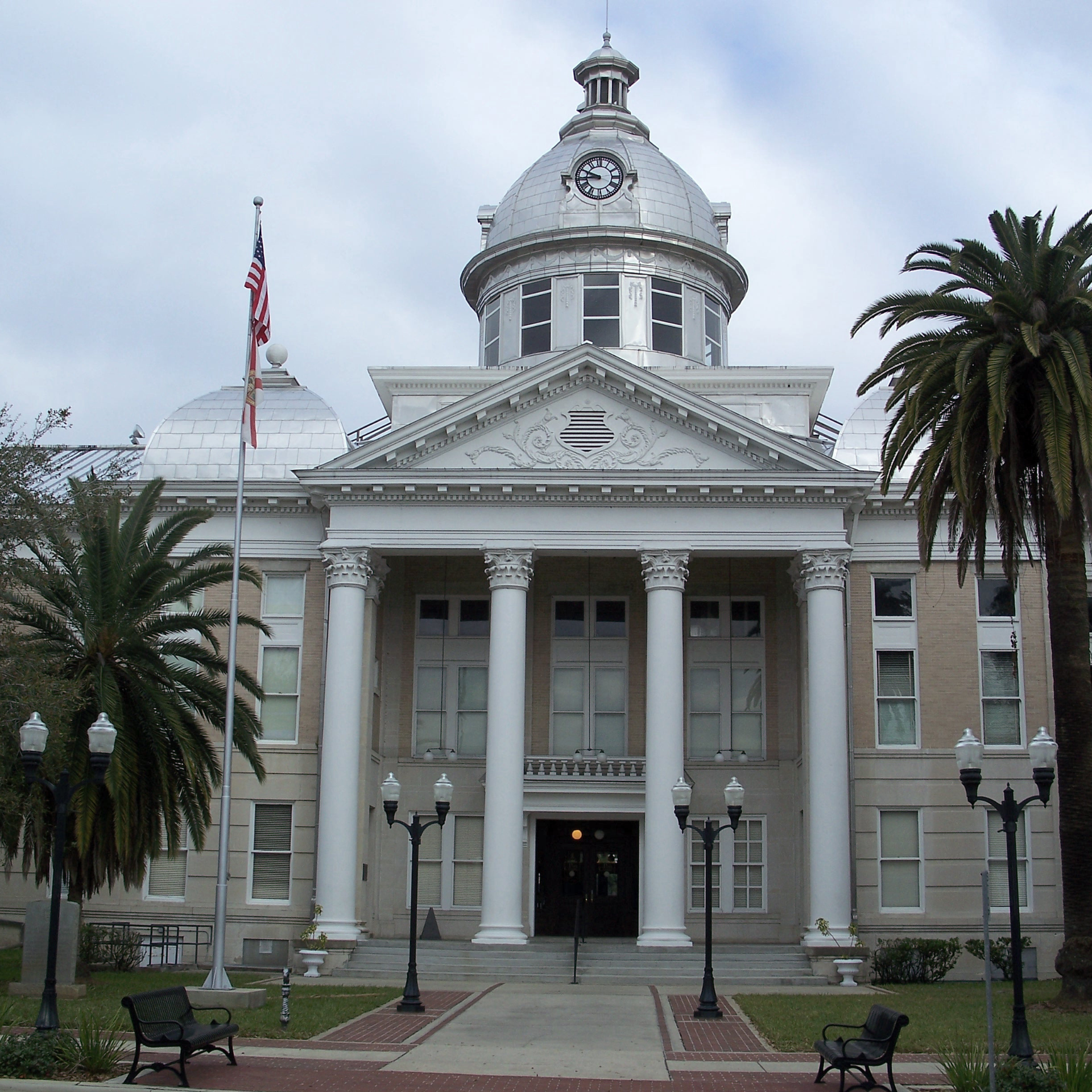A historic courthouse with a white domed clock tower, classic columns, and palm trees in a front courtyard.