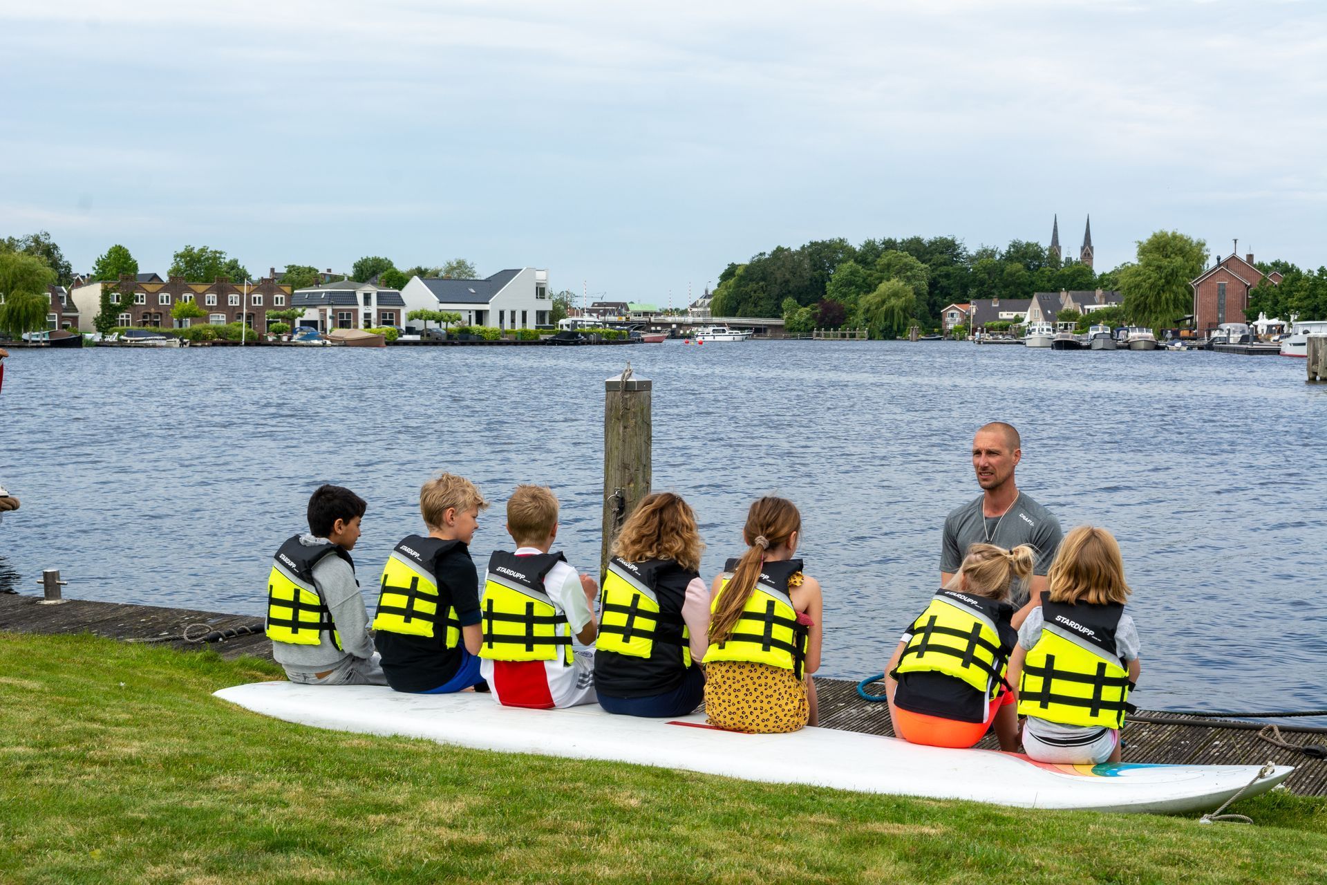 een groep kinderen zit op een surfplank naast een watermassa.