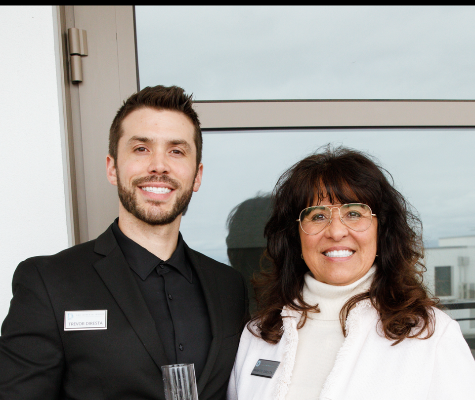 Modern kitchen with wood cabinets, white countertops, and dining table. Beige chairs and pendant lights.