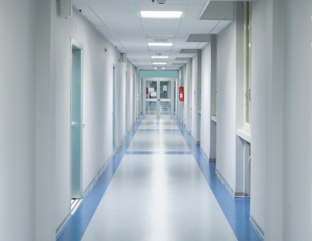 An empty hospital hallway with blue floors and white walls.