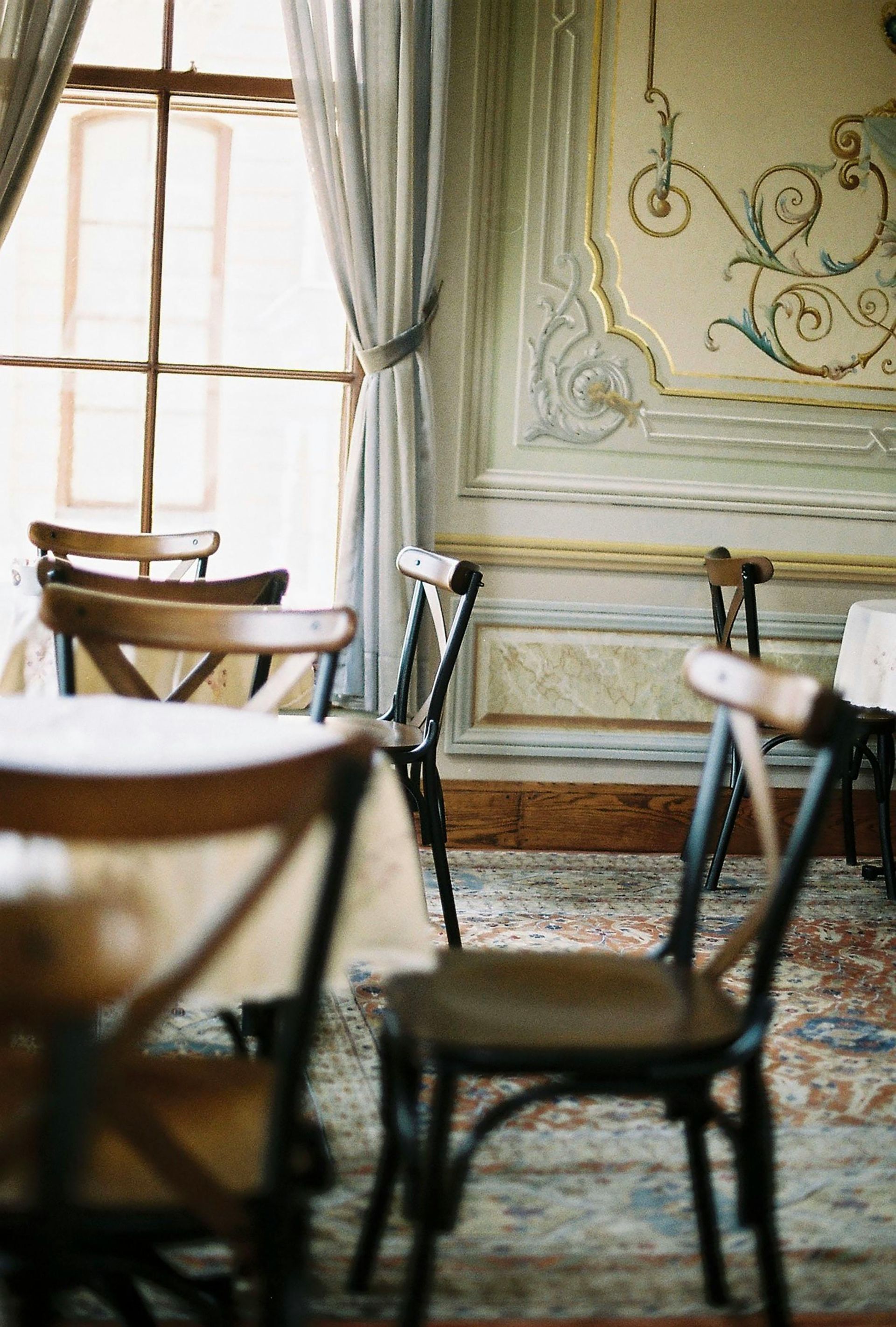 Dining room with wooden chairs, a patterned rug, and ornate wall details near a window.