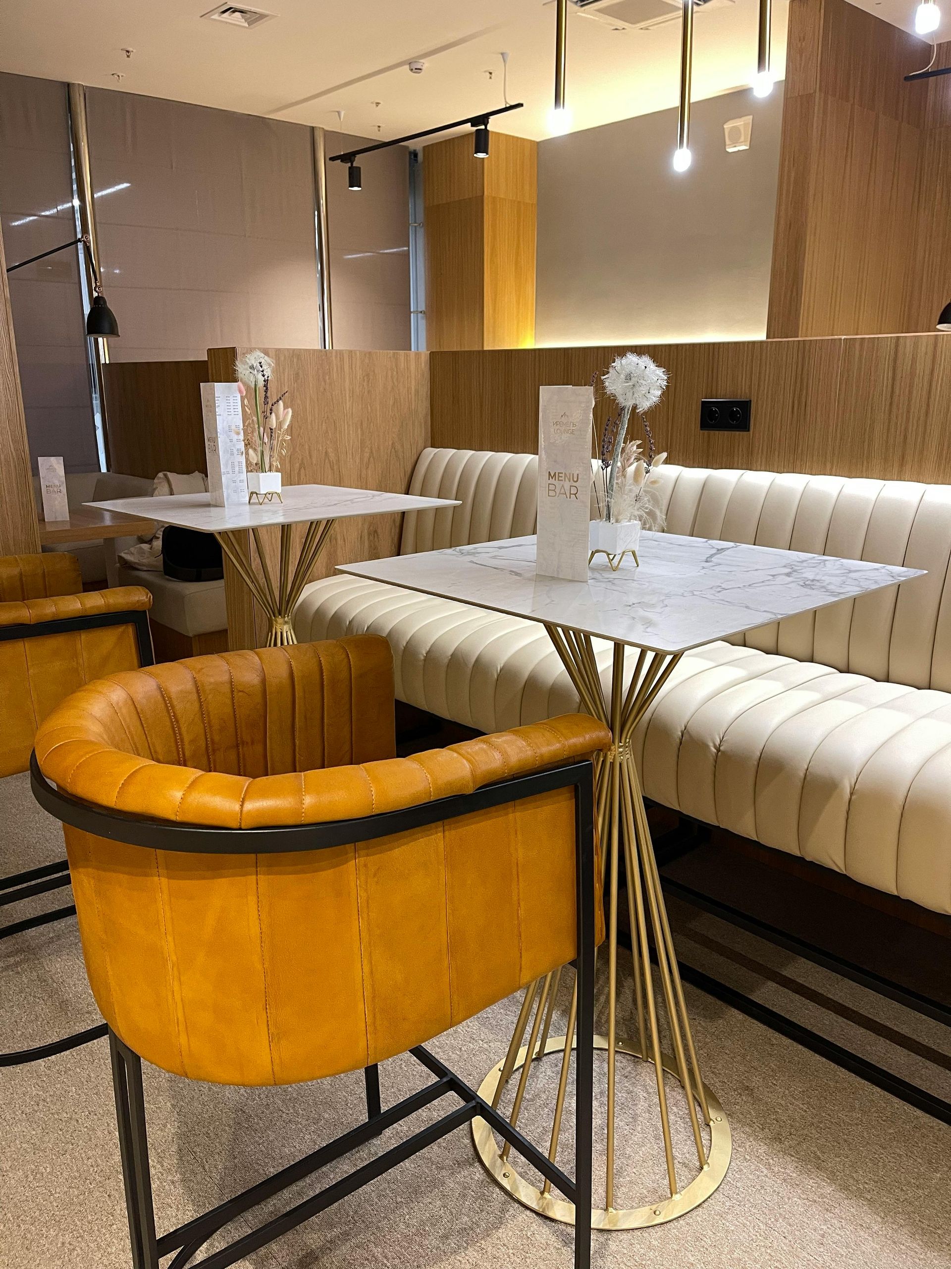 Yellow leather chair, white marble tables, and cream booth seating in a modern cafe with warm lighting.