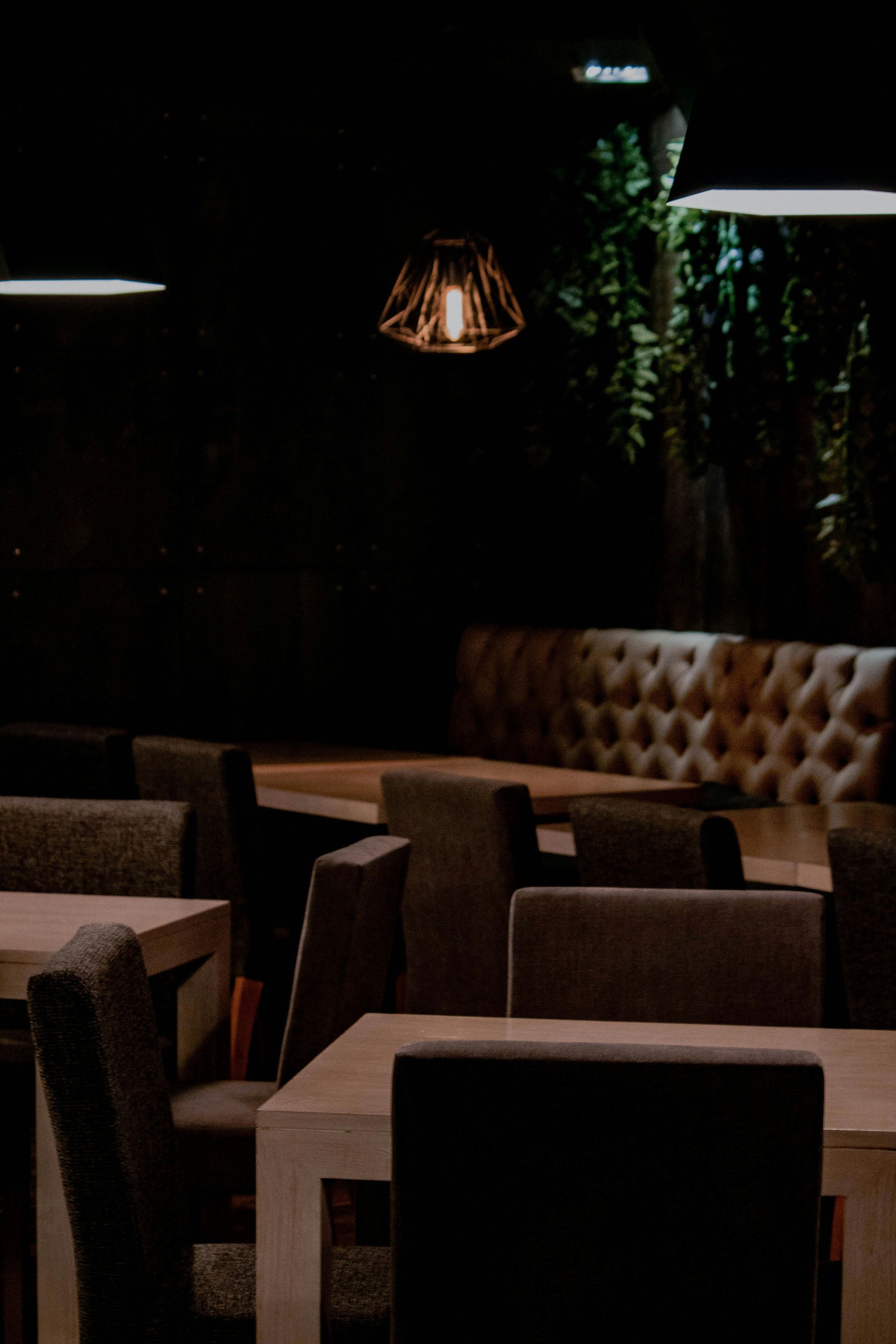 Dimly lit restaurant interior with tables, chairs, and a tufted booth. A hanging lamp illuminates the scene.