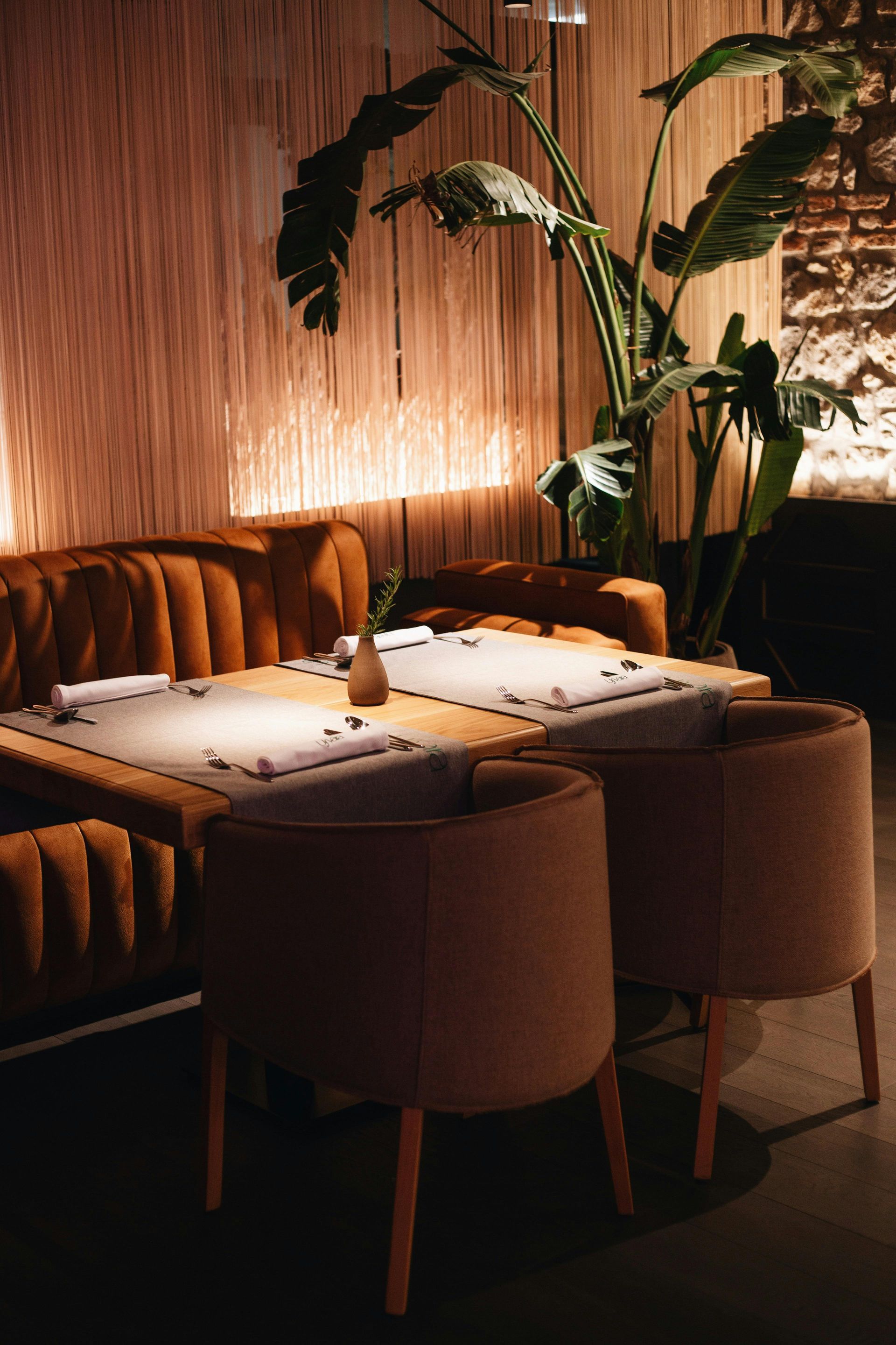 Cozy restaurant booth with orange upholstery, a table set for dining, and large tropical plant.