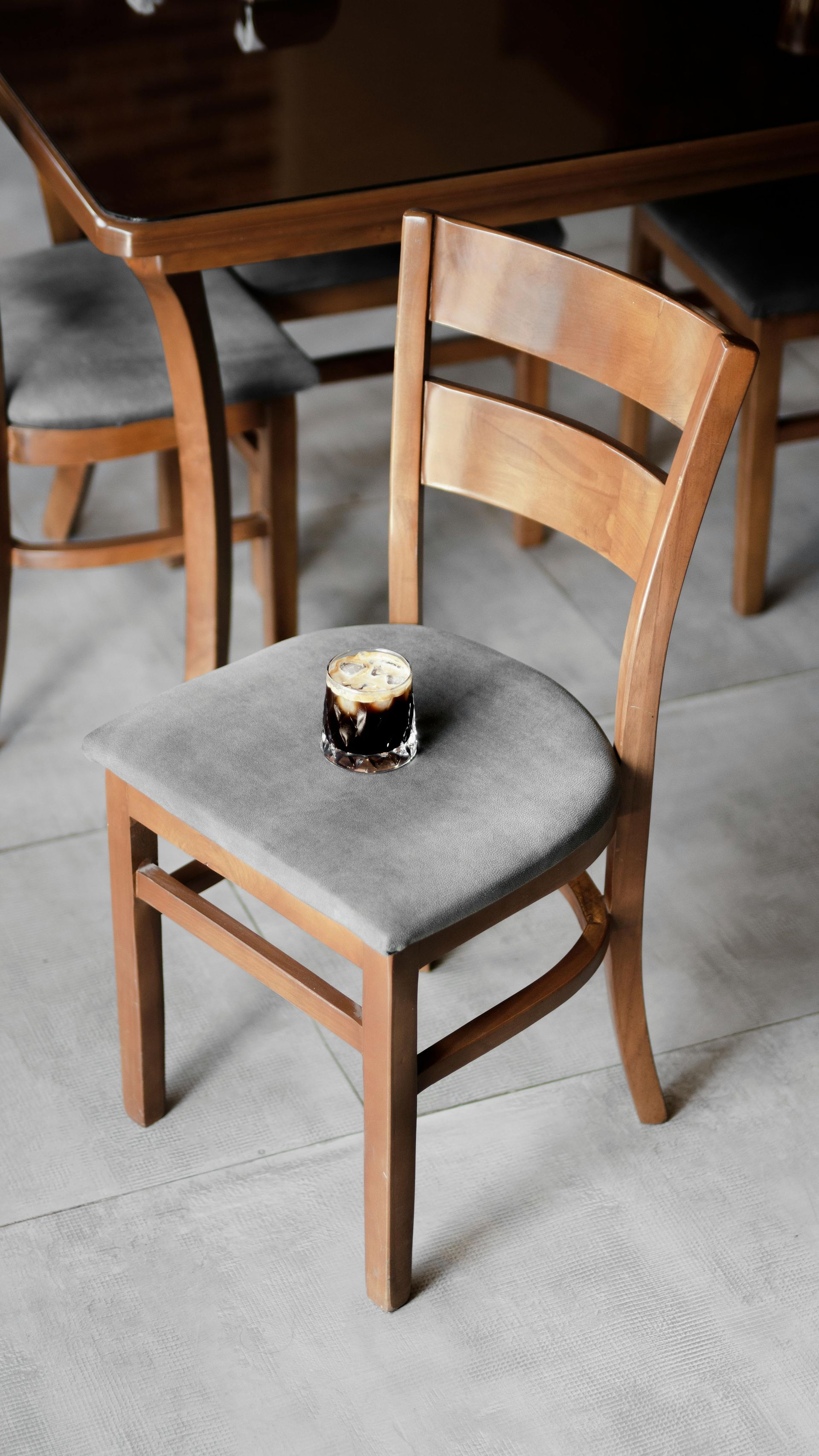 A glass of dark beer sits on a gray cushioned chair in a dining room setting.