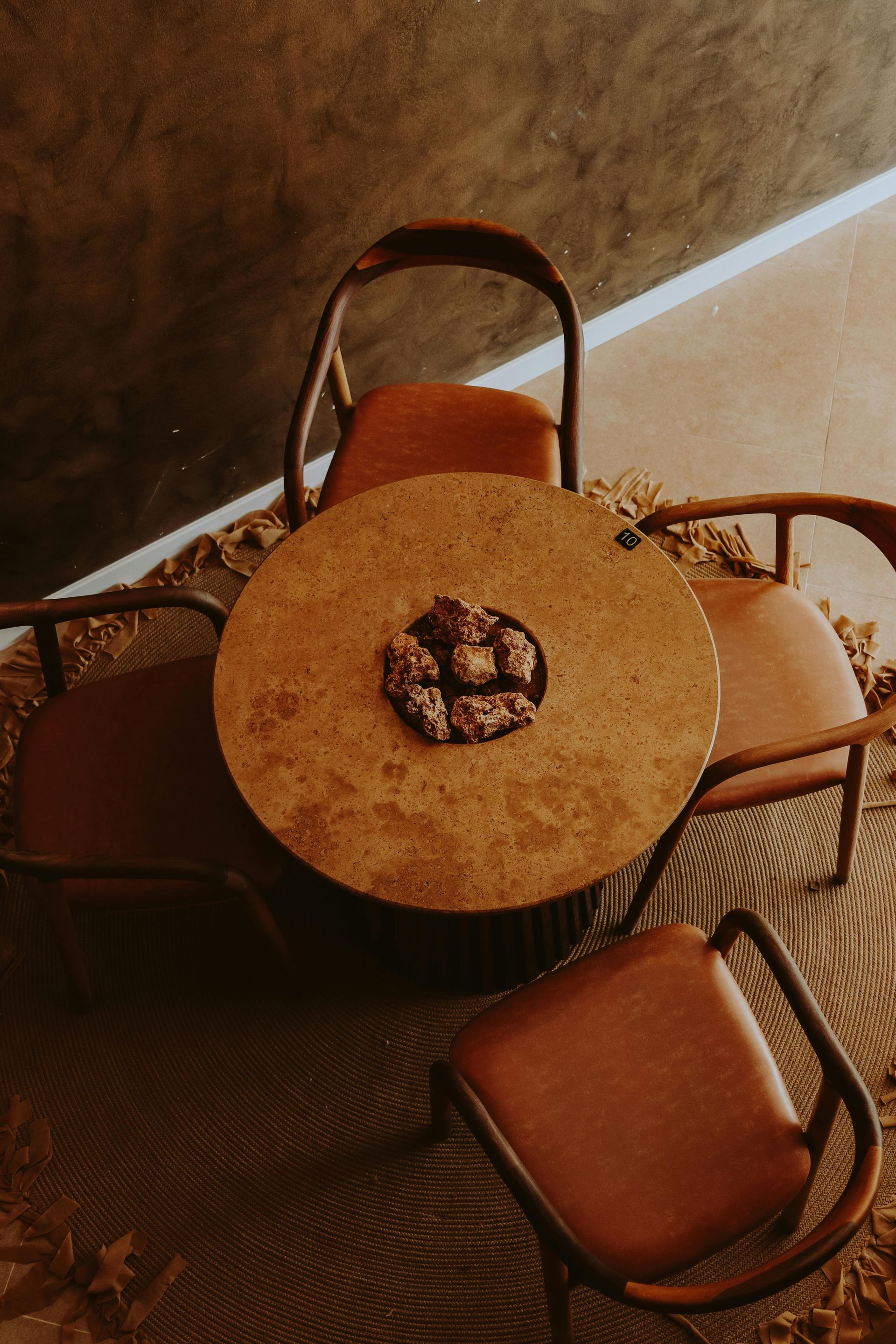 Round table with four brown chairs and decorative centerpieces, on a woven rug.