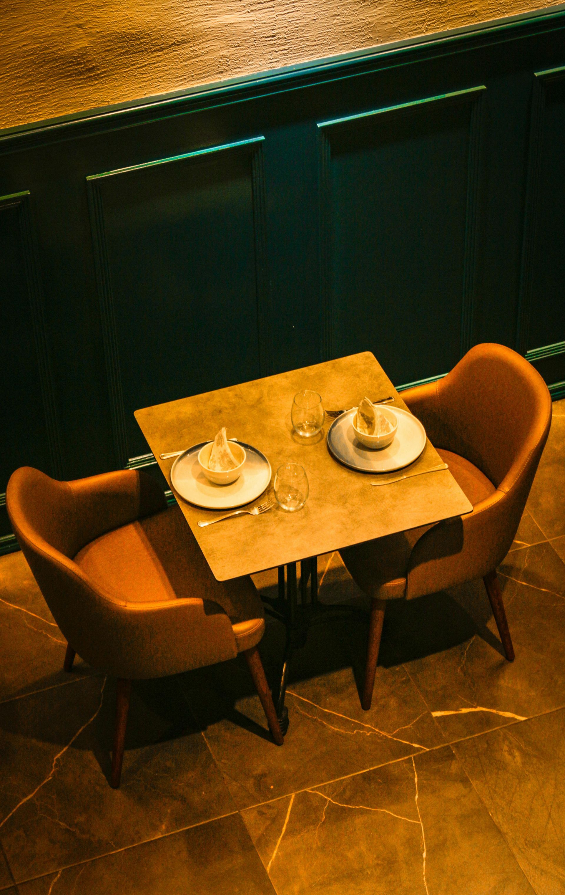 Two chairs face a table set for two in a dimly lit, upscale restaurant.