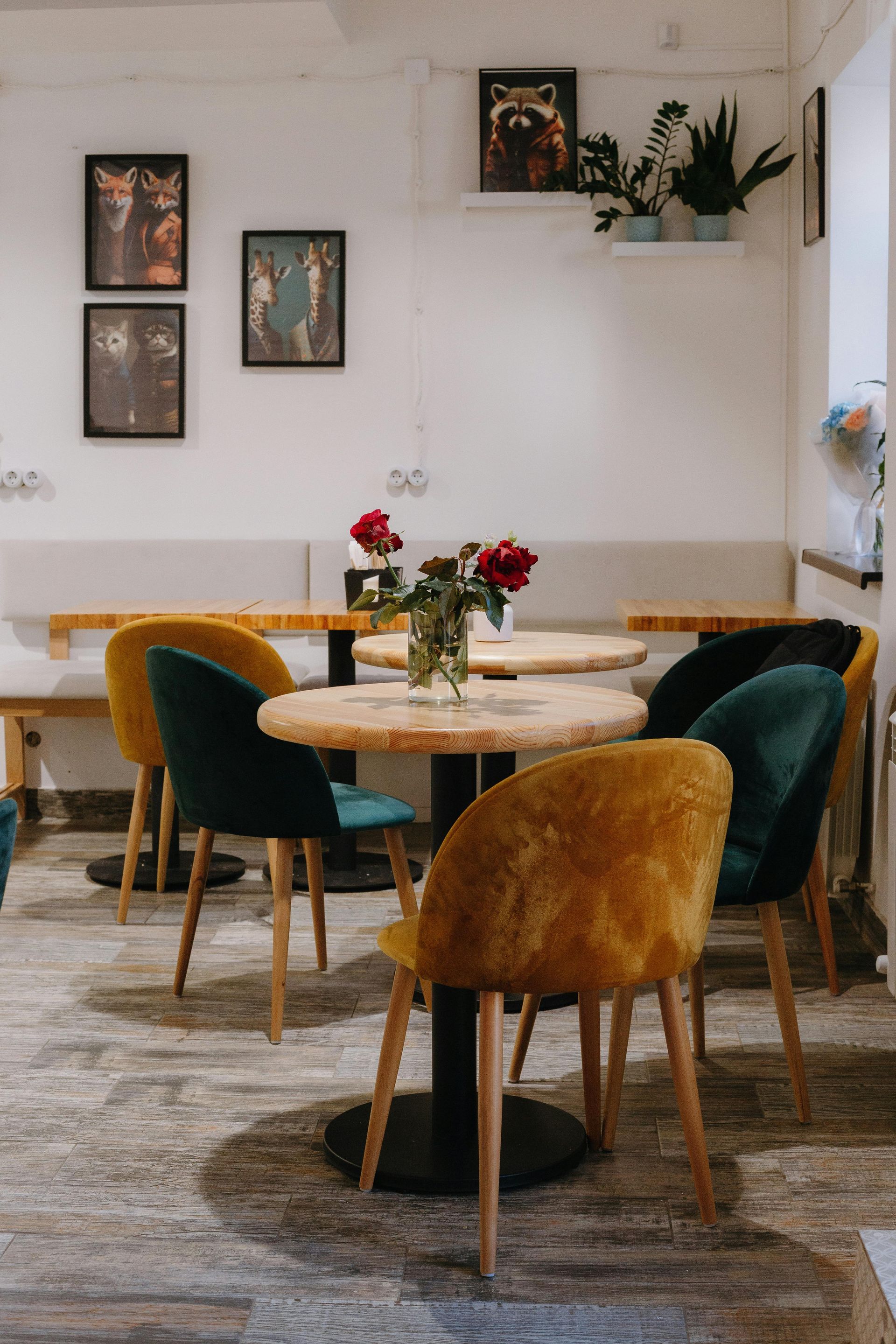 Cafe interior with round tables, colorful velvet chairs, artwork, and a vase of flowers.