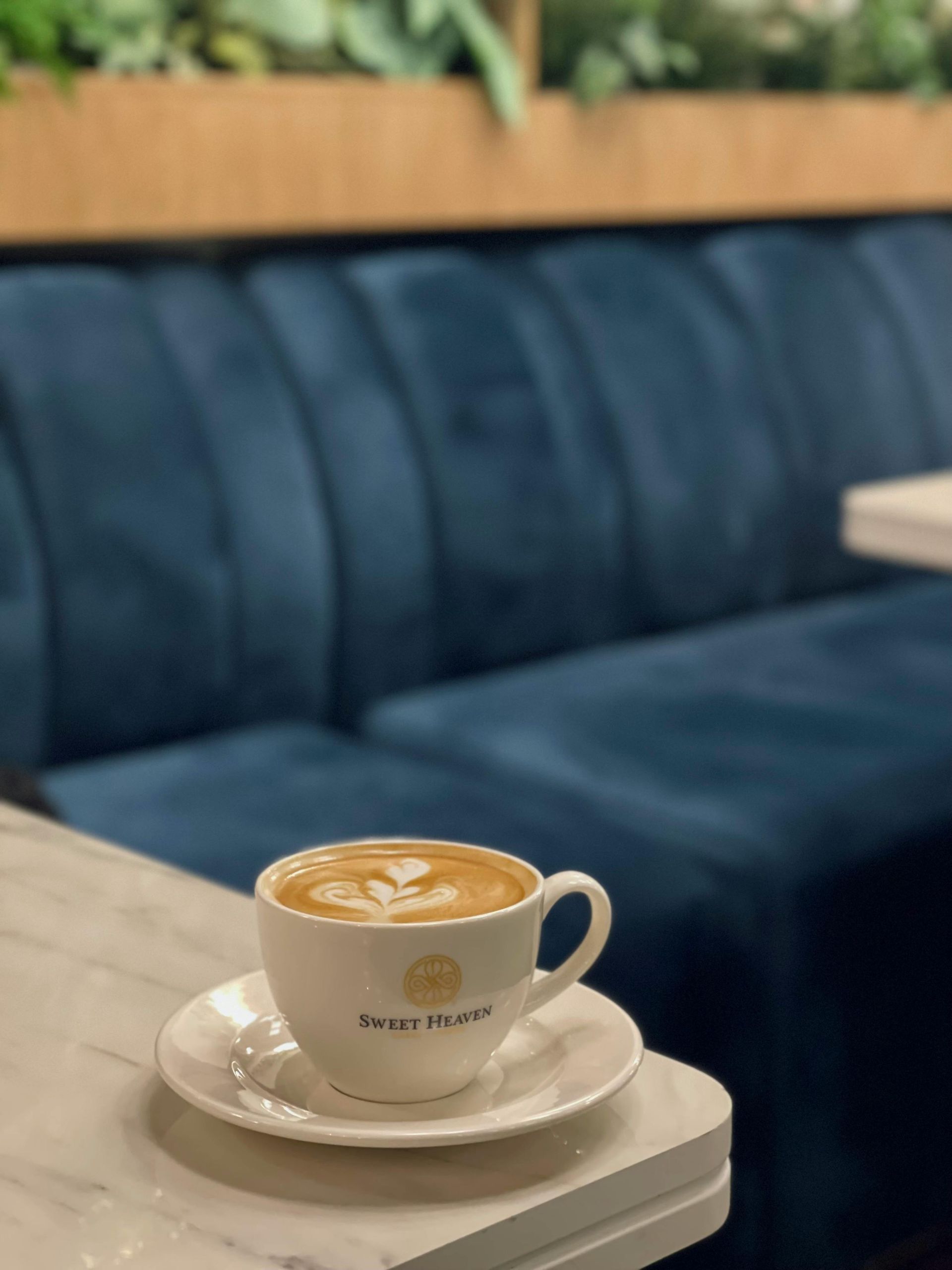 Latte in a white cup with latte art on a marble-topped table, with blue velvet seating in the background.