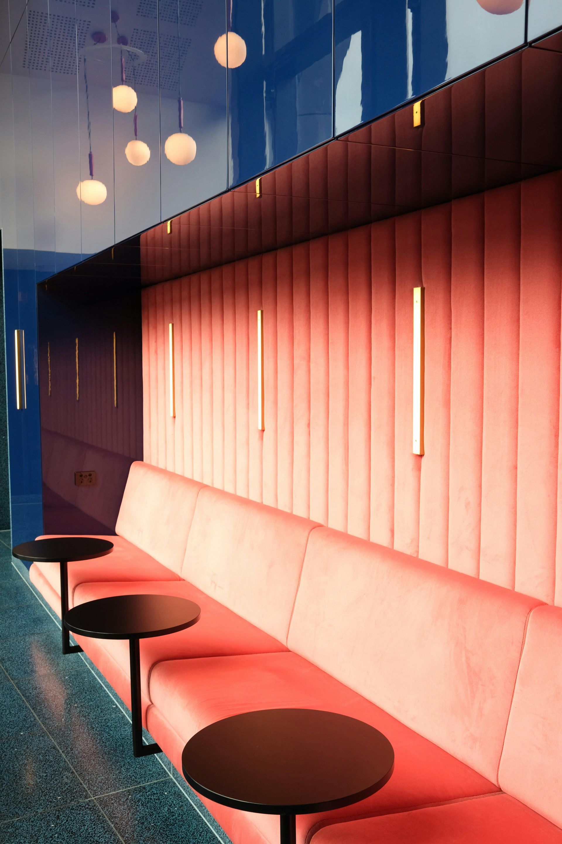 Red booth seating with black tables, against a blue wall with hanging lights.