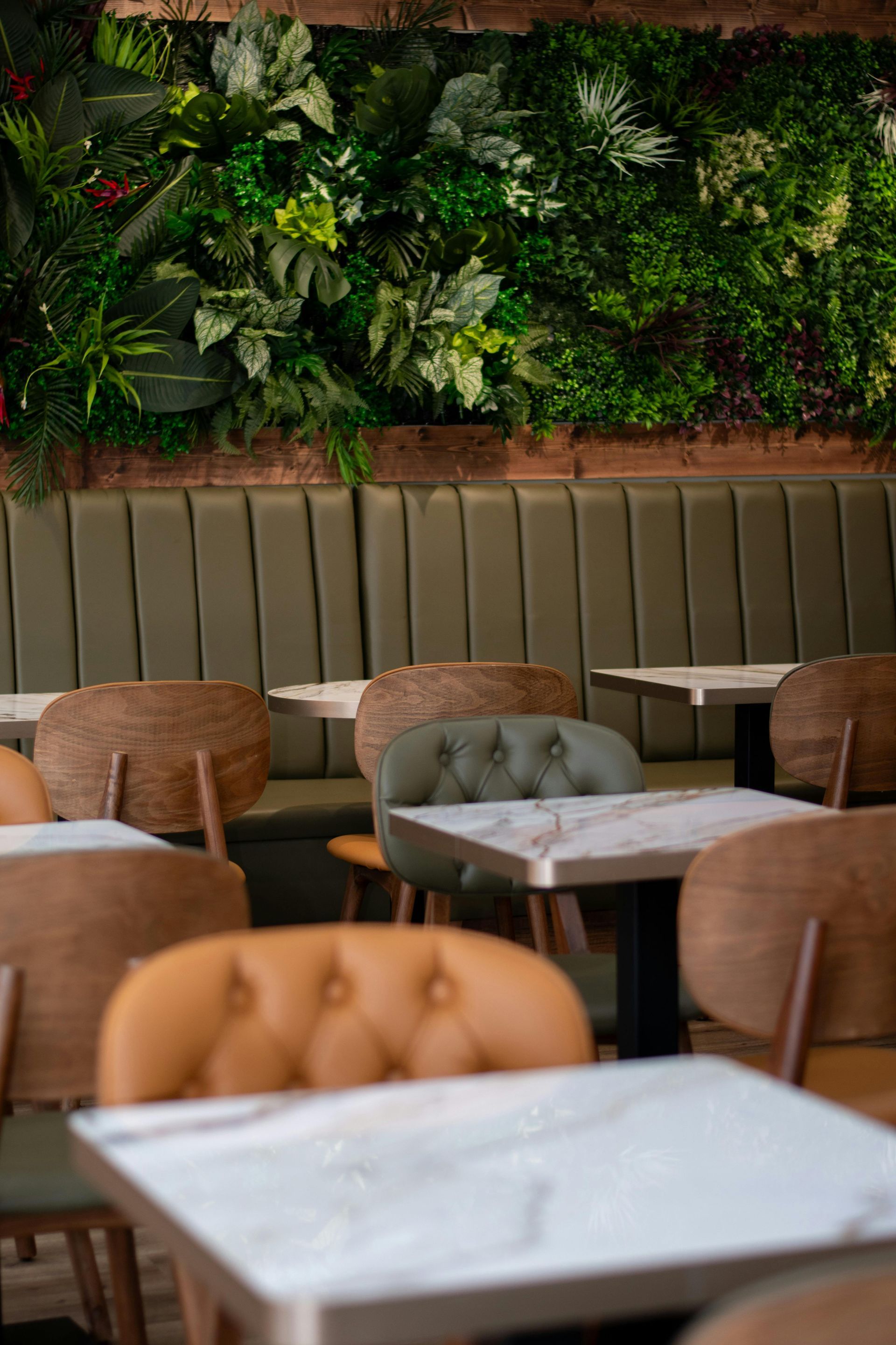 Restaurant interior with green plant wall, booth seating, and tables with marble tops.