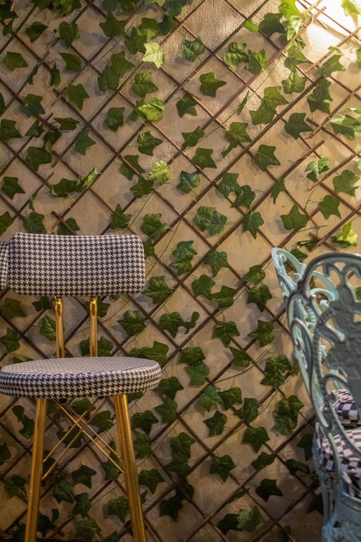 Chair with houndstooth seat, next to blue chair, against a wall covered in faux ivy.