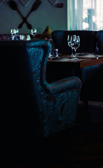 Cozy restaurant seating with ornate blue chairs, set tables, and crossed kitchen utensils on the wall.