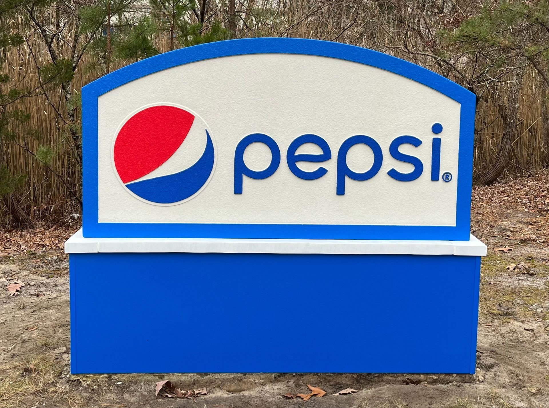 Pepsi sign with the brand's logo: red and blue globe, white background, blue base, outdoors.