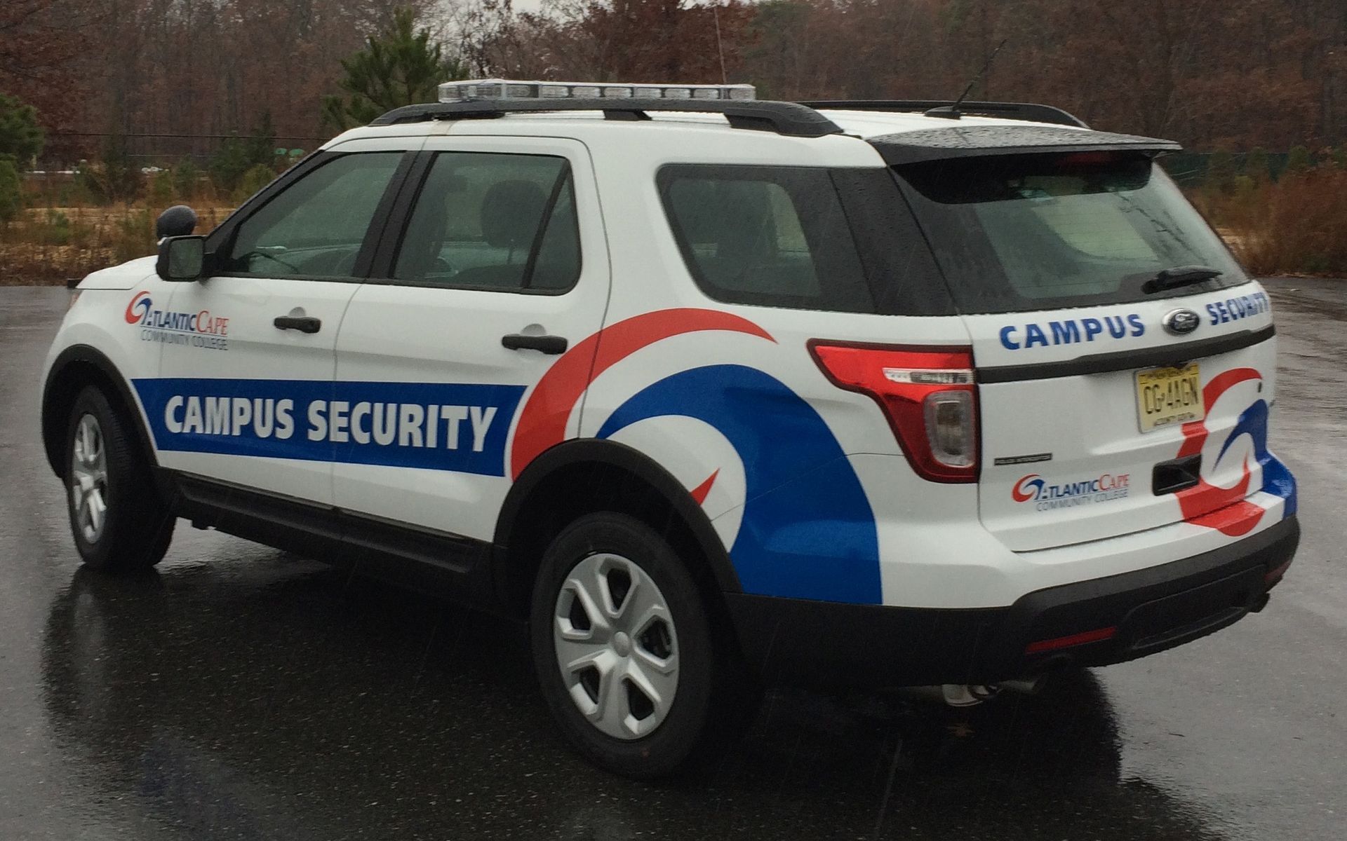 White and blue campus security SUV parked on wet pavement; logo on side and back.