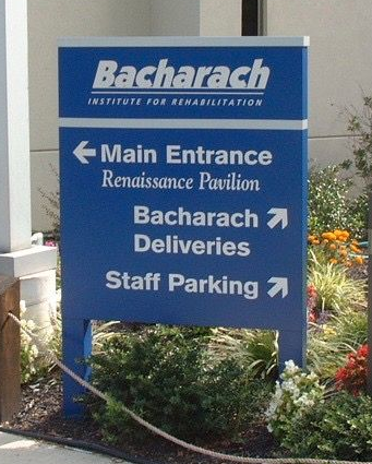 Blue directional sign for Bacharach Institute, with arrows pointing to Main Entrance, Deliveries, and Staff Parking.