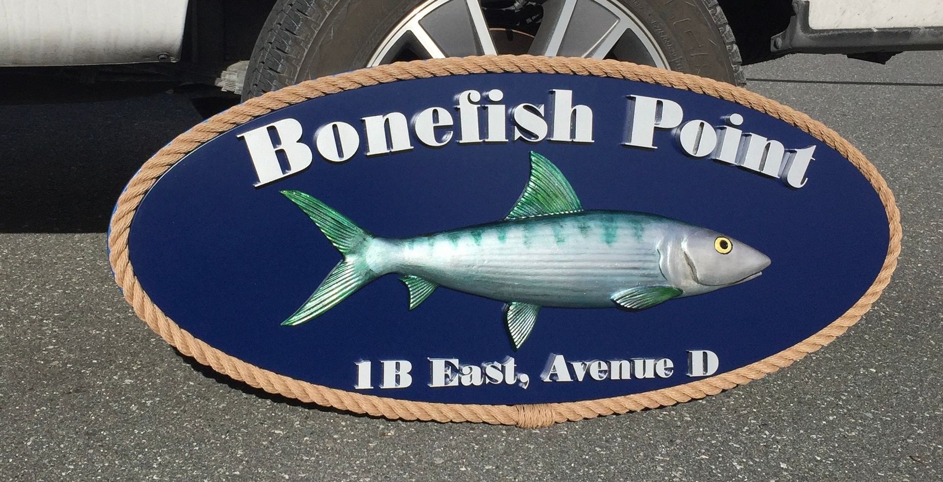 Oval sign for Bonefish Point, with a blue background, a fish illustration, and text, trimmed with rope.