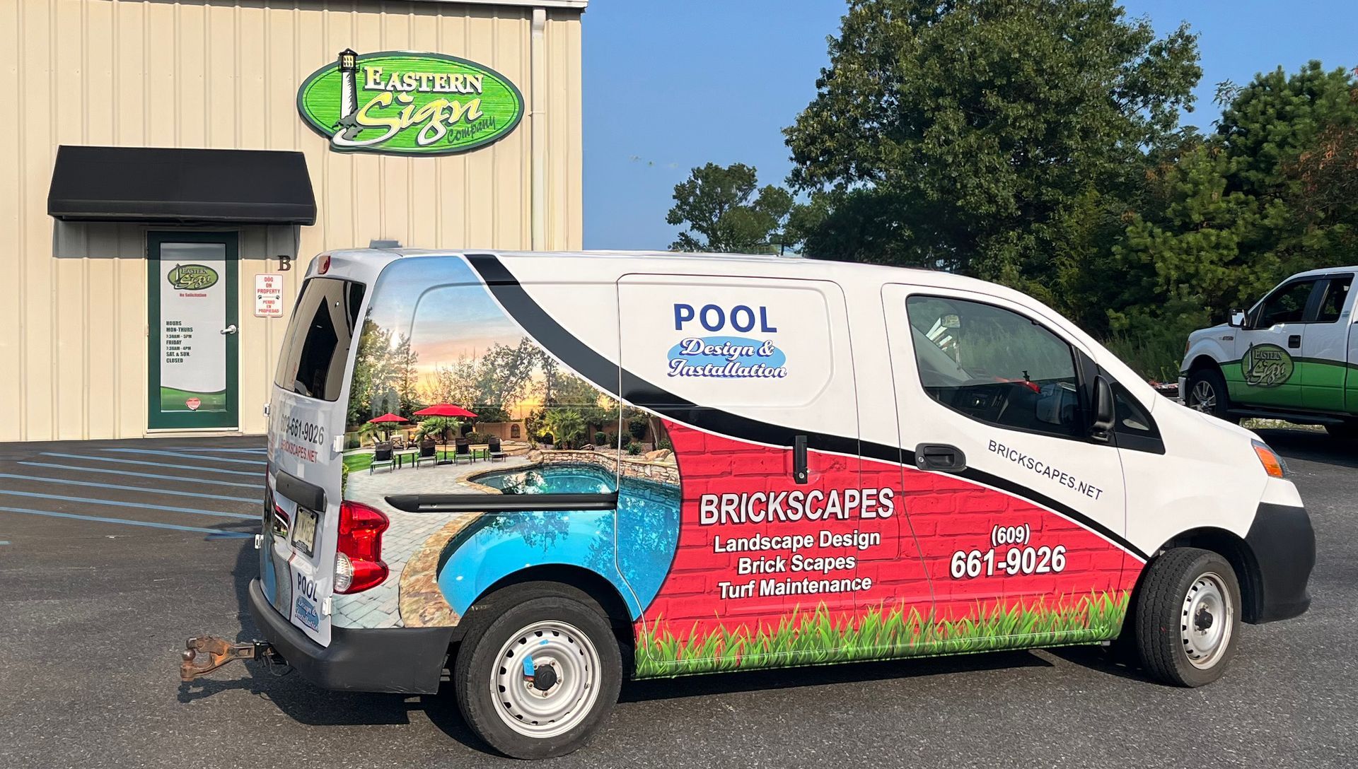 White van with pool and landscaping advertisement parked in front of a business with a green sign.