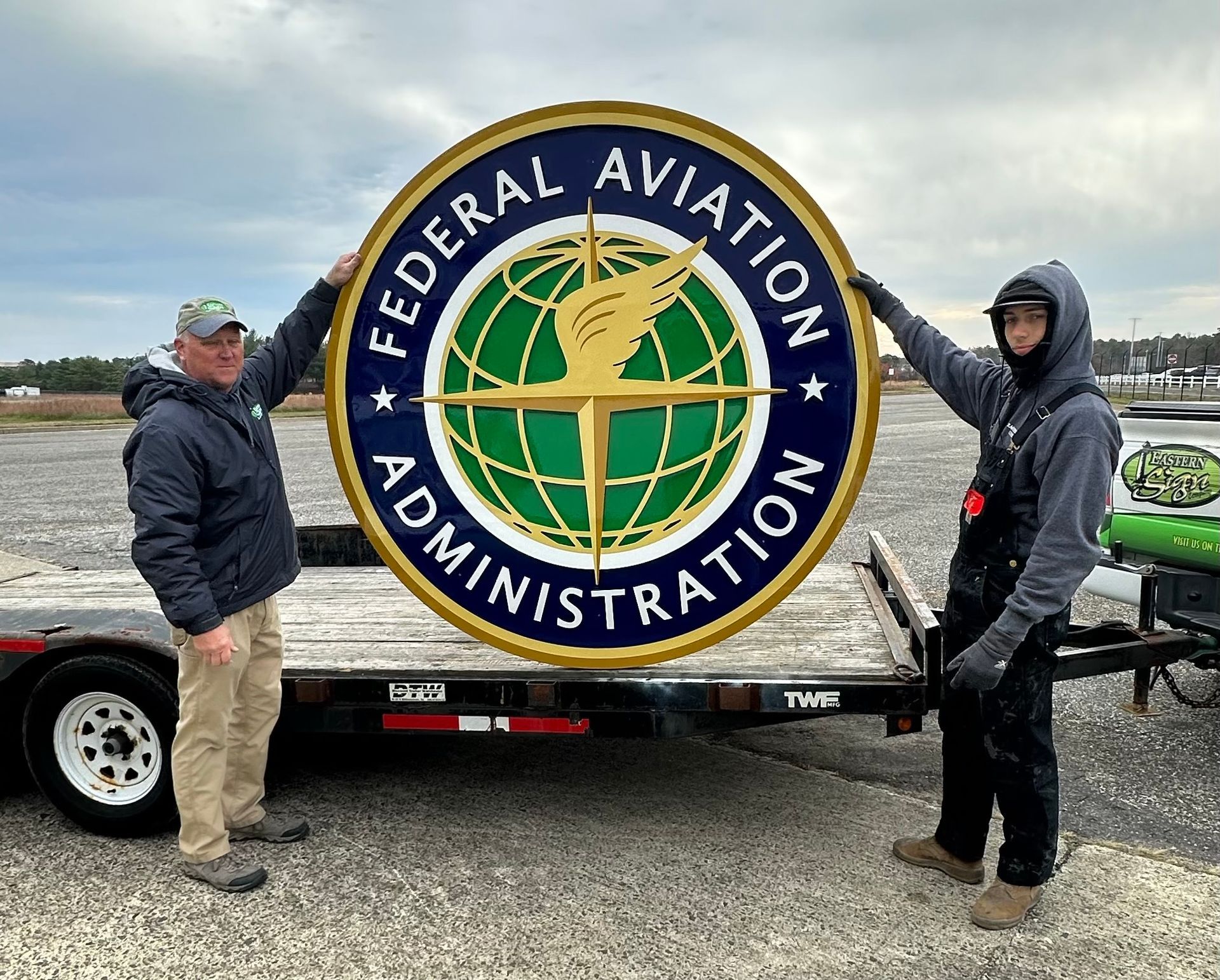 Two people holding a large Federal Aviation Administration sign on a trailer.