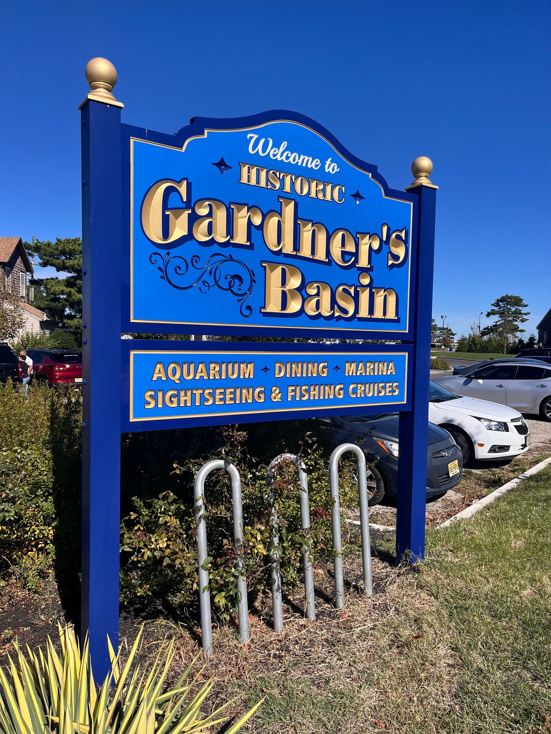Sign for Gardner's Basin, Atlantic City. Blue and gold sign lists aquarium, dining, and cruises. Bicycle rack in front.