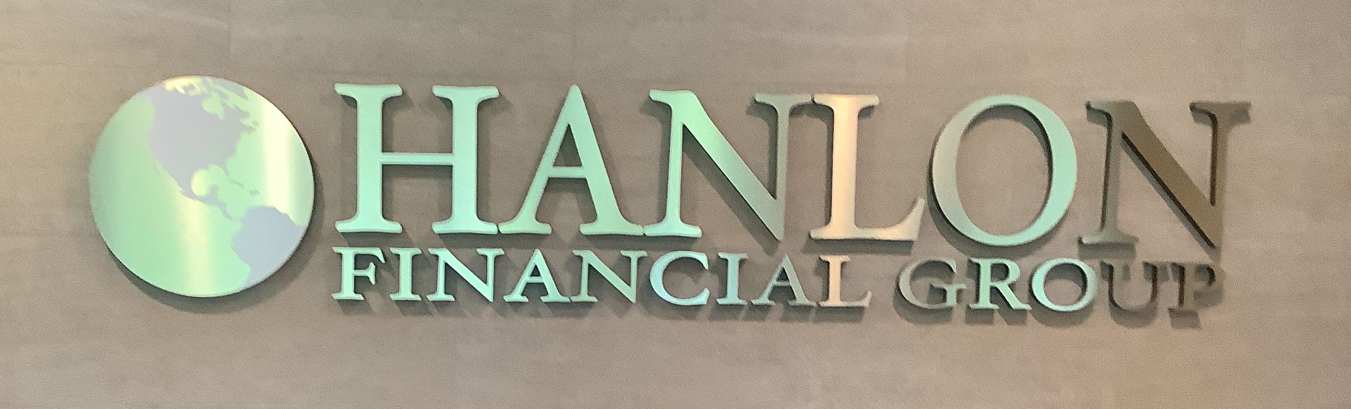Hanlon Financial Group logo with globe icon. Green and silver lettering on light grey wall.