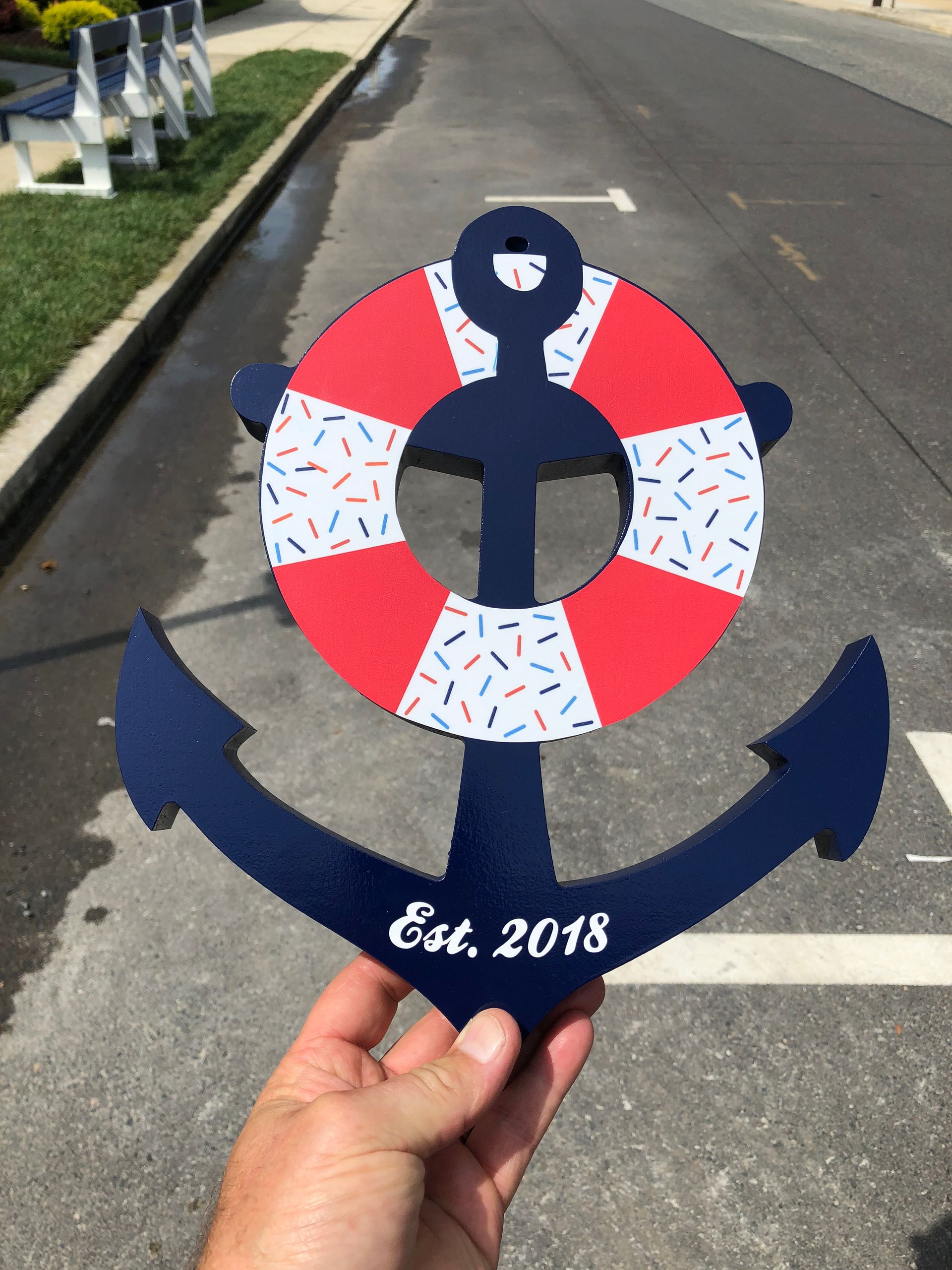 Blue anchor with a red and white life preserver, held by a hand; 