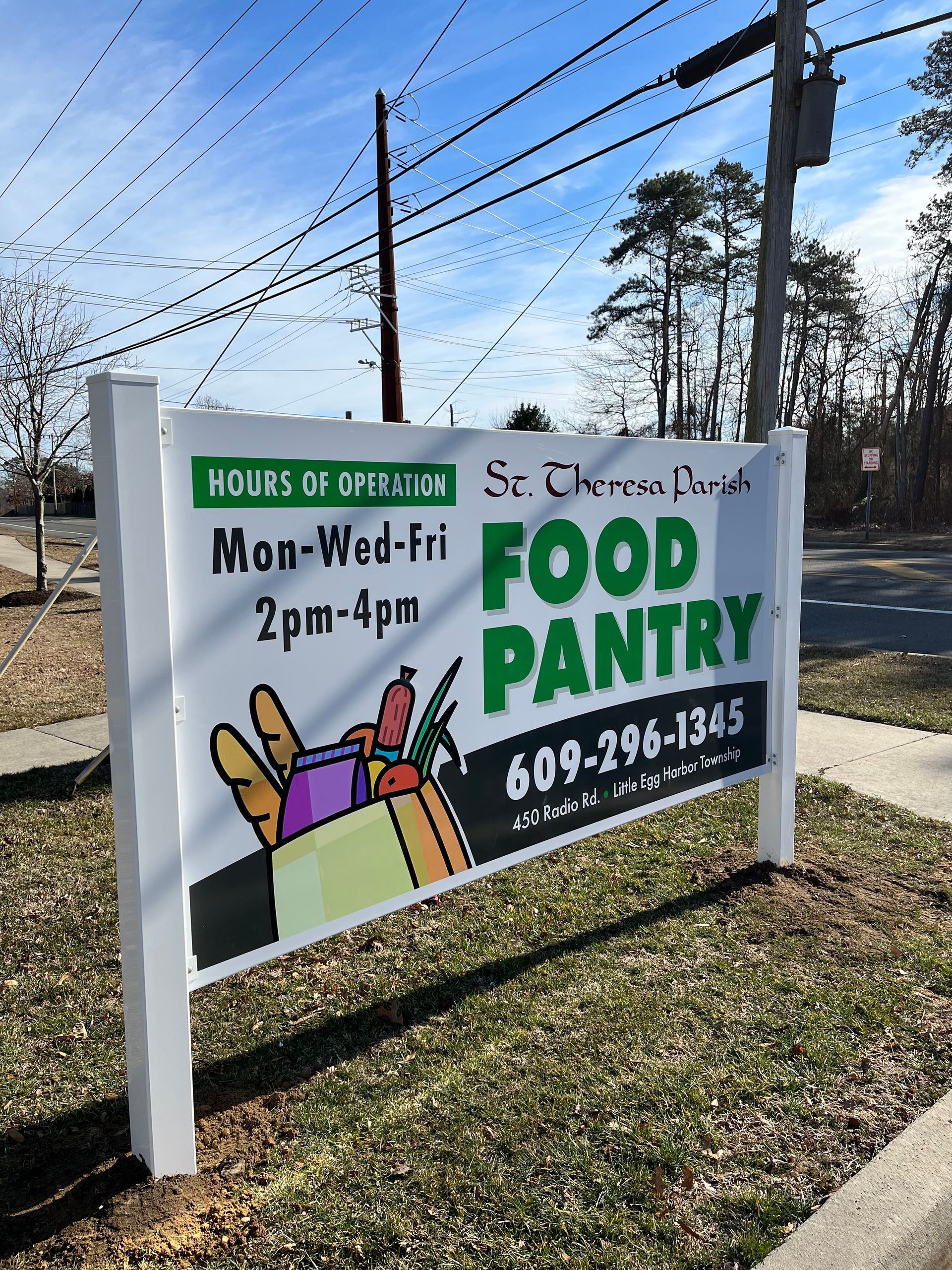 Sign for St. Therese Parish Food Pantry with hours: Mon-Wed-Fri 2-4pm, phone number 609-296-1345, graphic of a shopping bag.