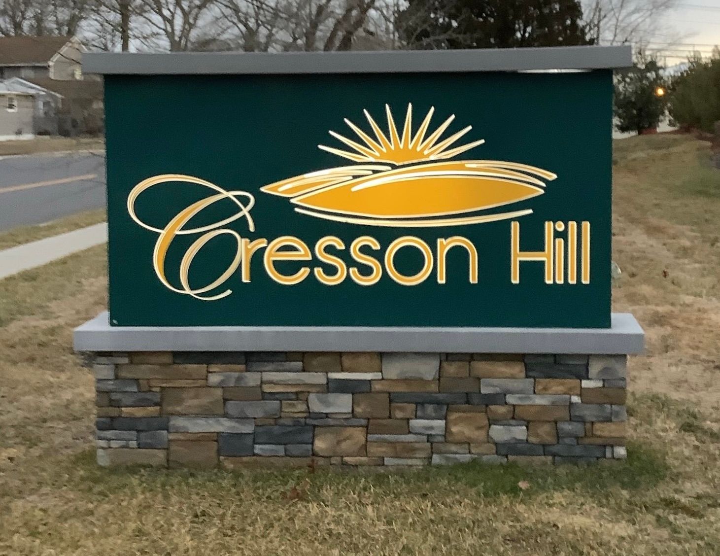 Cresson Hill sign, green background, gold lettering, stone base, sun logo.