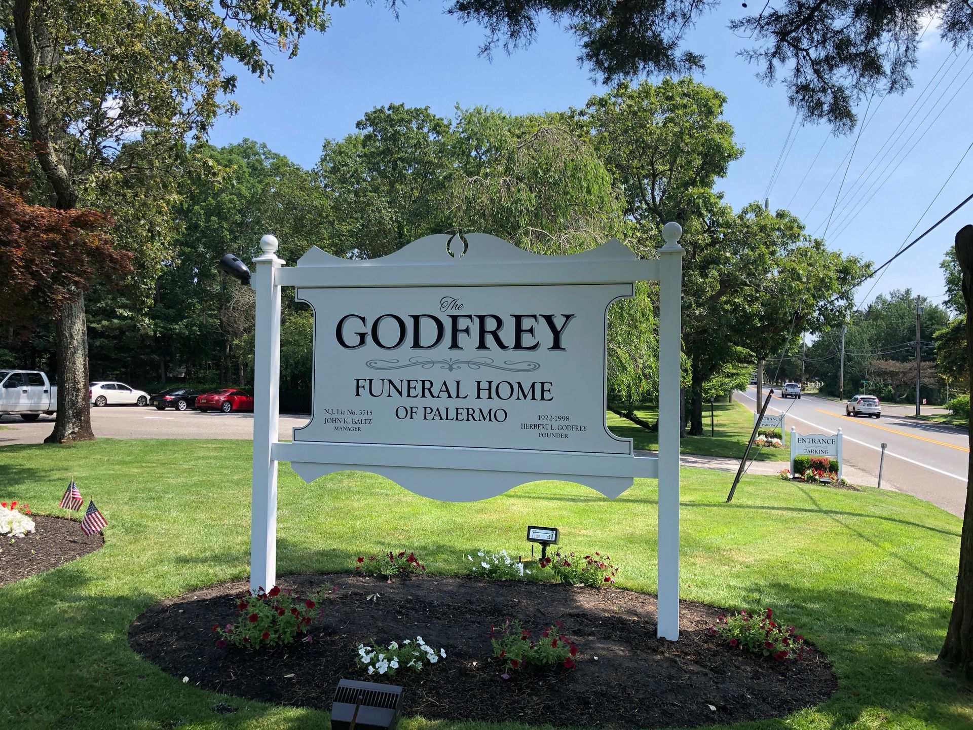 Sign for Godfrey Funeral Home, white with black text, in front of a green lawn and trees.