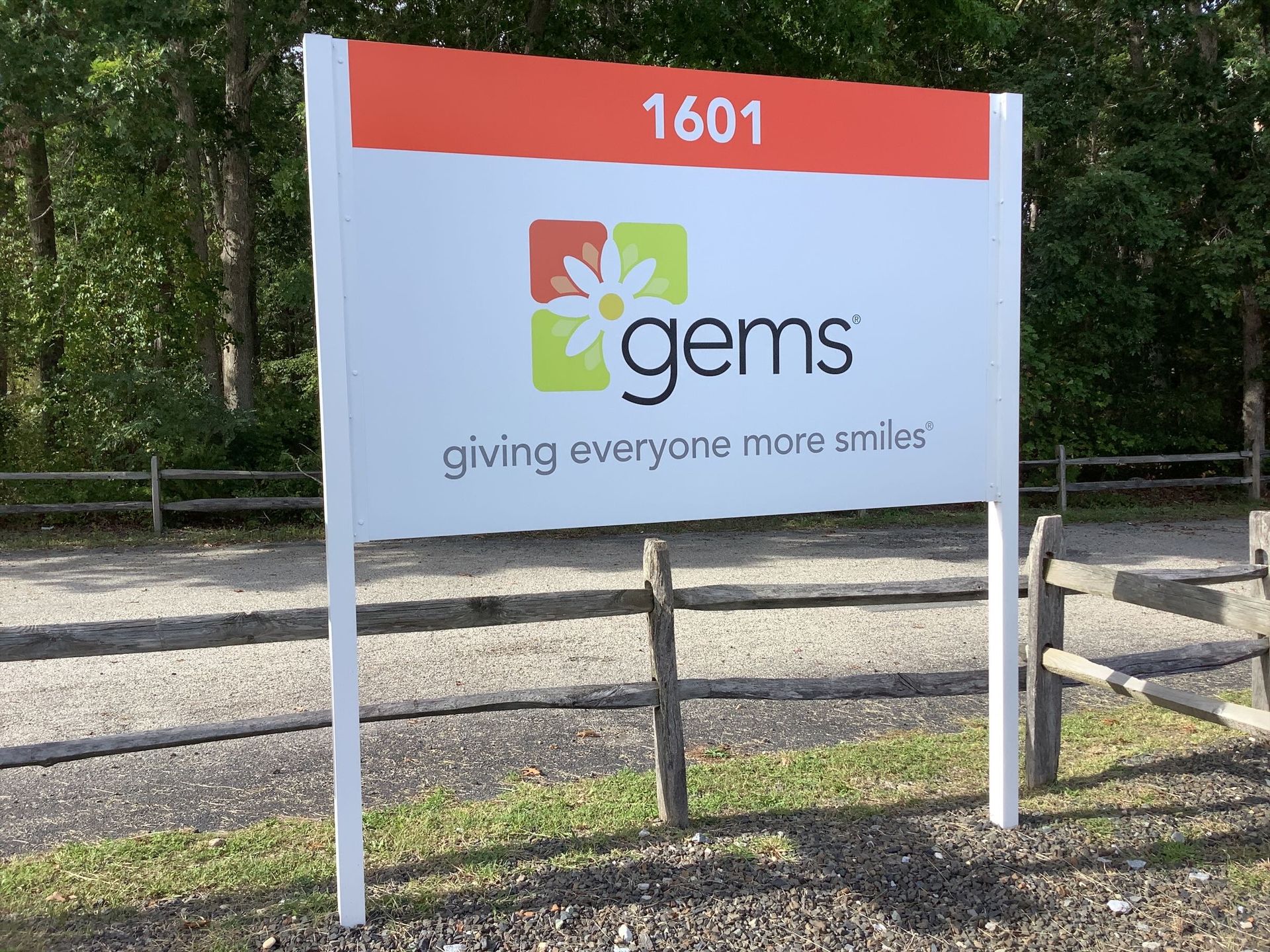 Sign for GEMS at 1601 with logo, orange top, and giving everyone more smiles tagline.