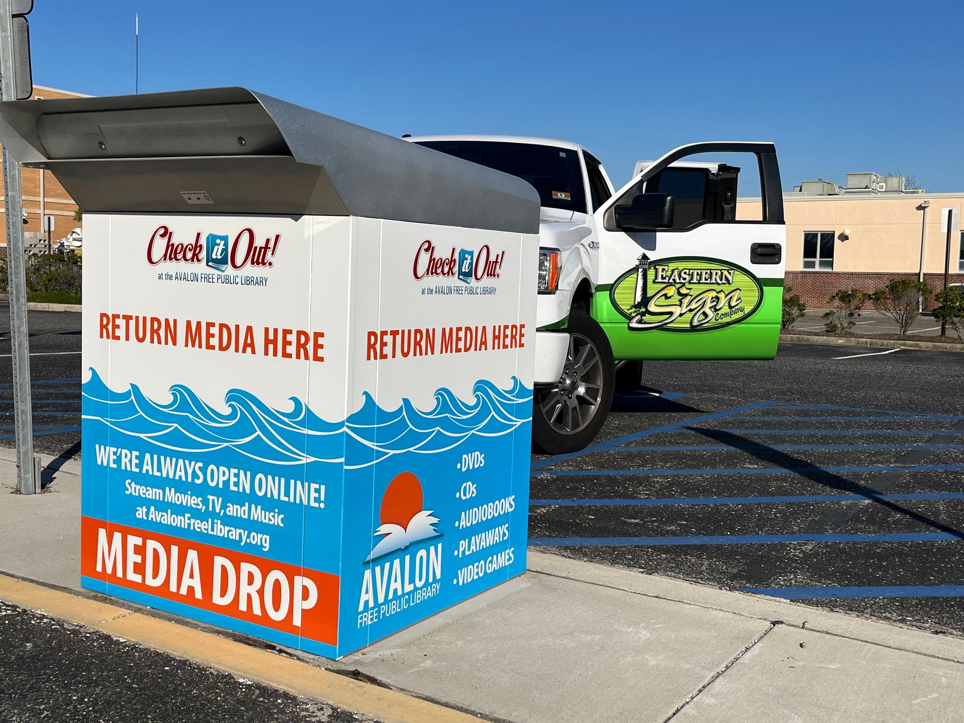 White truck with open door next to a blue and white media drop box.