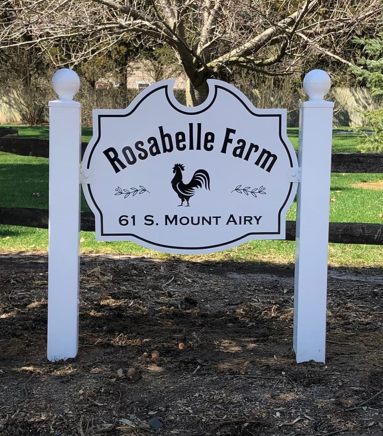 Sign for Rosabelle Farm, white posts, black text, rooster image, address 