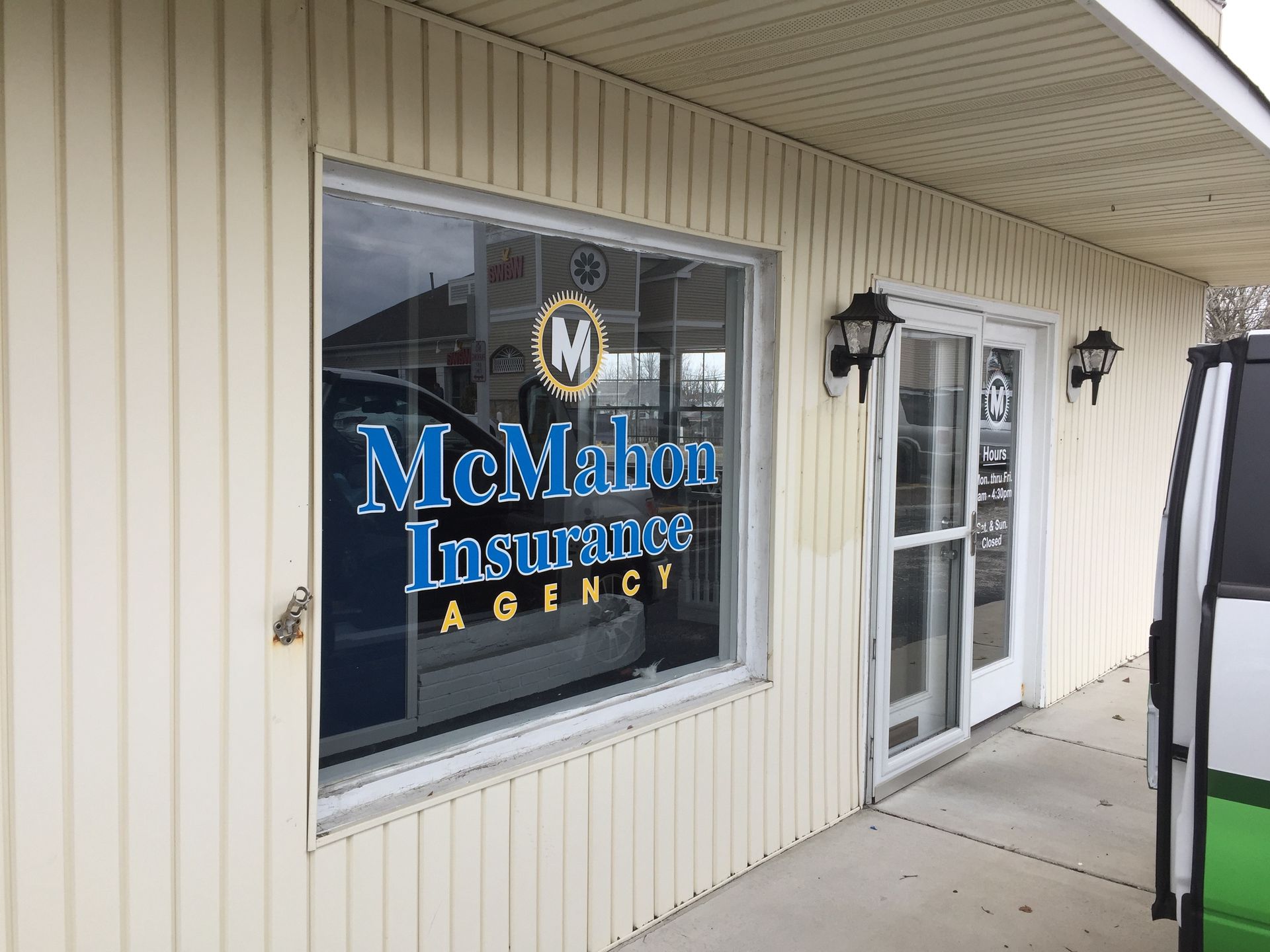 Exterior of McMahon Insurance Agency office with sign in the window and a white van to the right.