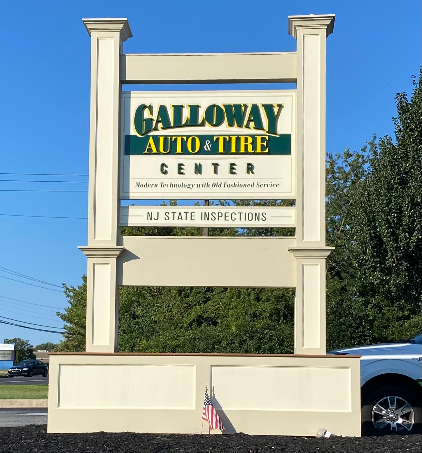 Sign for Galloway Auto & Tire Center, green and gold lettering, with beige frame, on a sunny day.