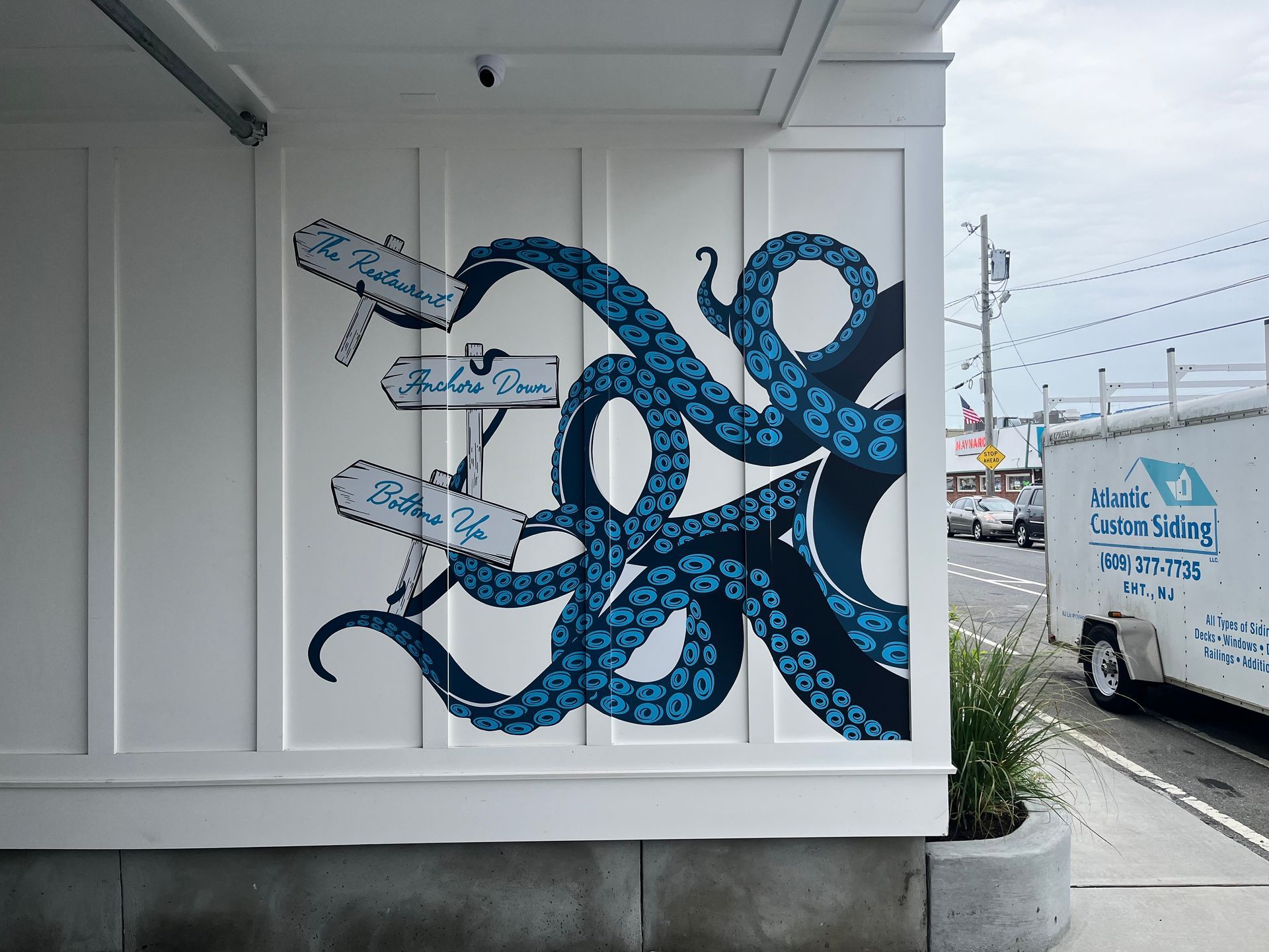 Mural of blue octopus tentacles wrapping around street signs on white wall.