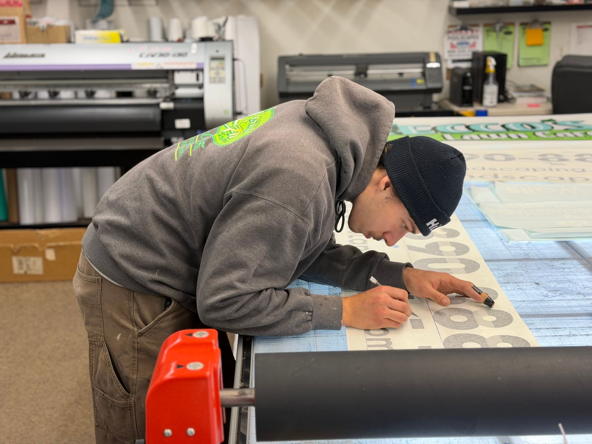 Person wearing a beanie and hoodie carefully working on a large print in a workshop setting.