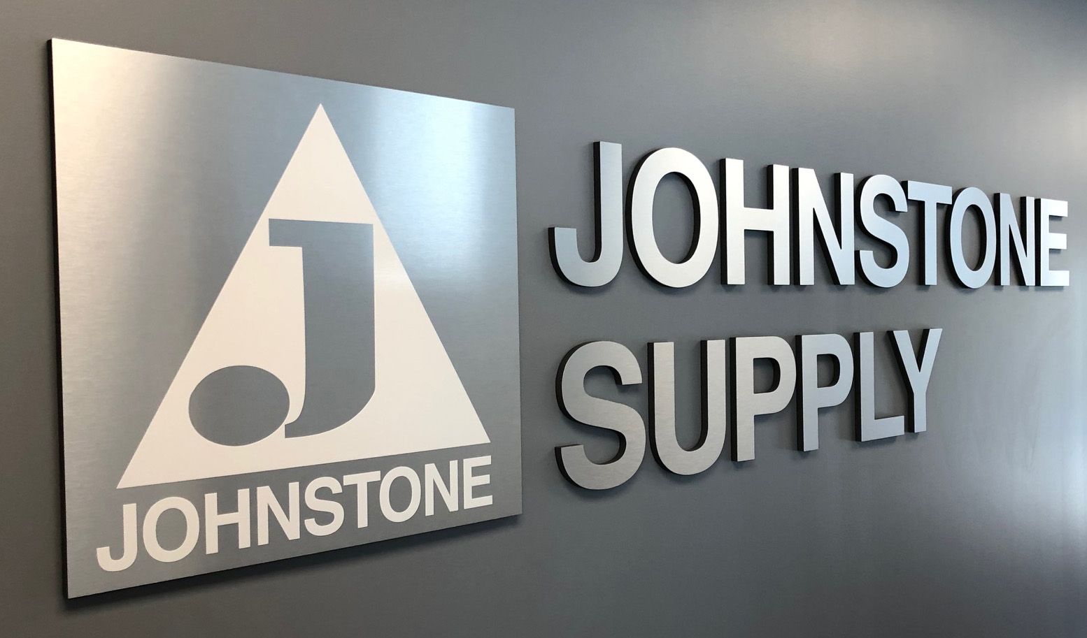 Johnstone Supply sign with a silver logo on a gray wall.