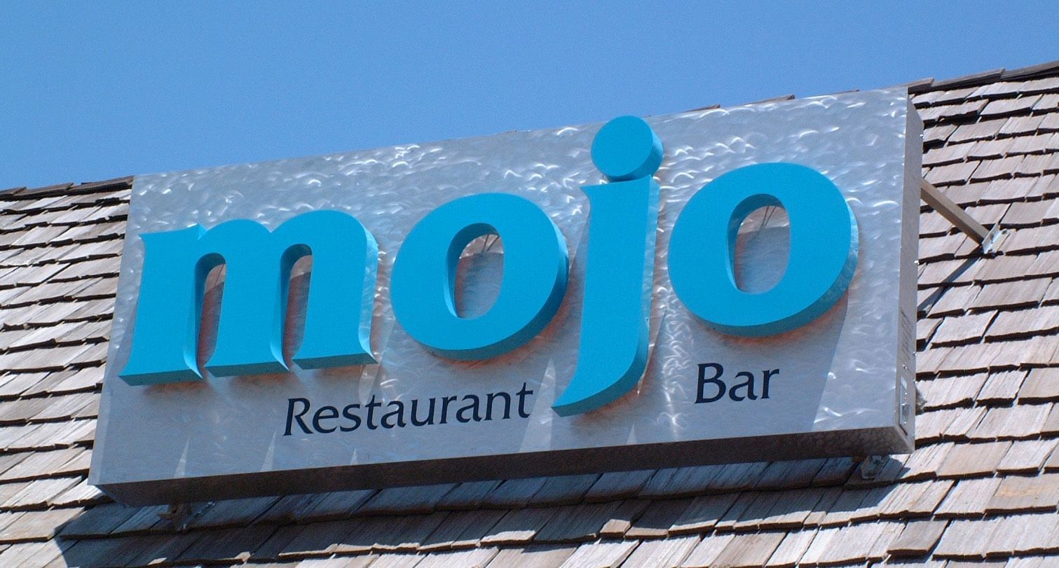 Mojo Restaurant Bar sign in turquoise on a textured silver background, mounted on a wooden shingled roof.