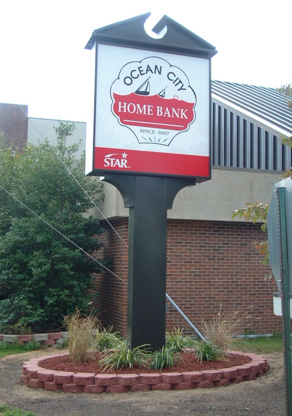 Sign for Ocean City Home Bank, white and red logo on a black post with brick base, Ocean City.
