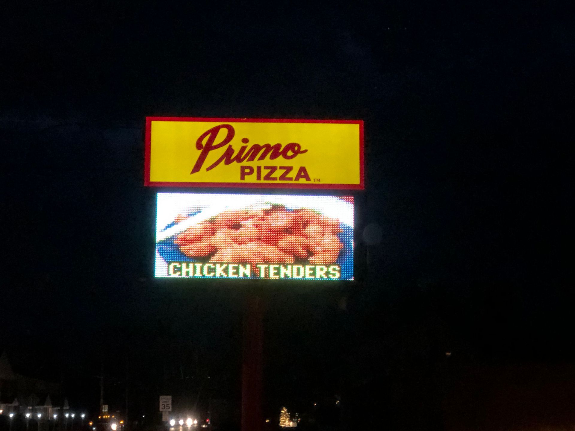Primo Pizza sign at night, yellow top with logo, LED display showing chicken tenders.