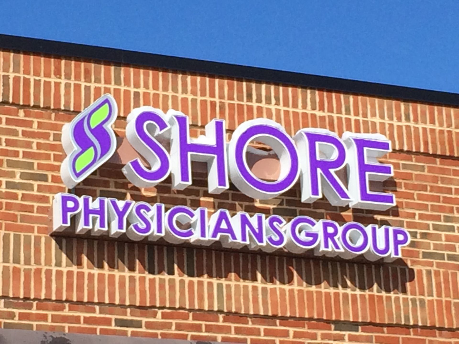 Shore Physicians Group sign on brick building, purple and white lettering.