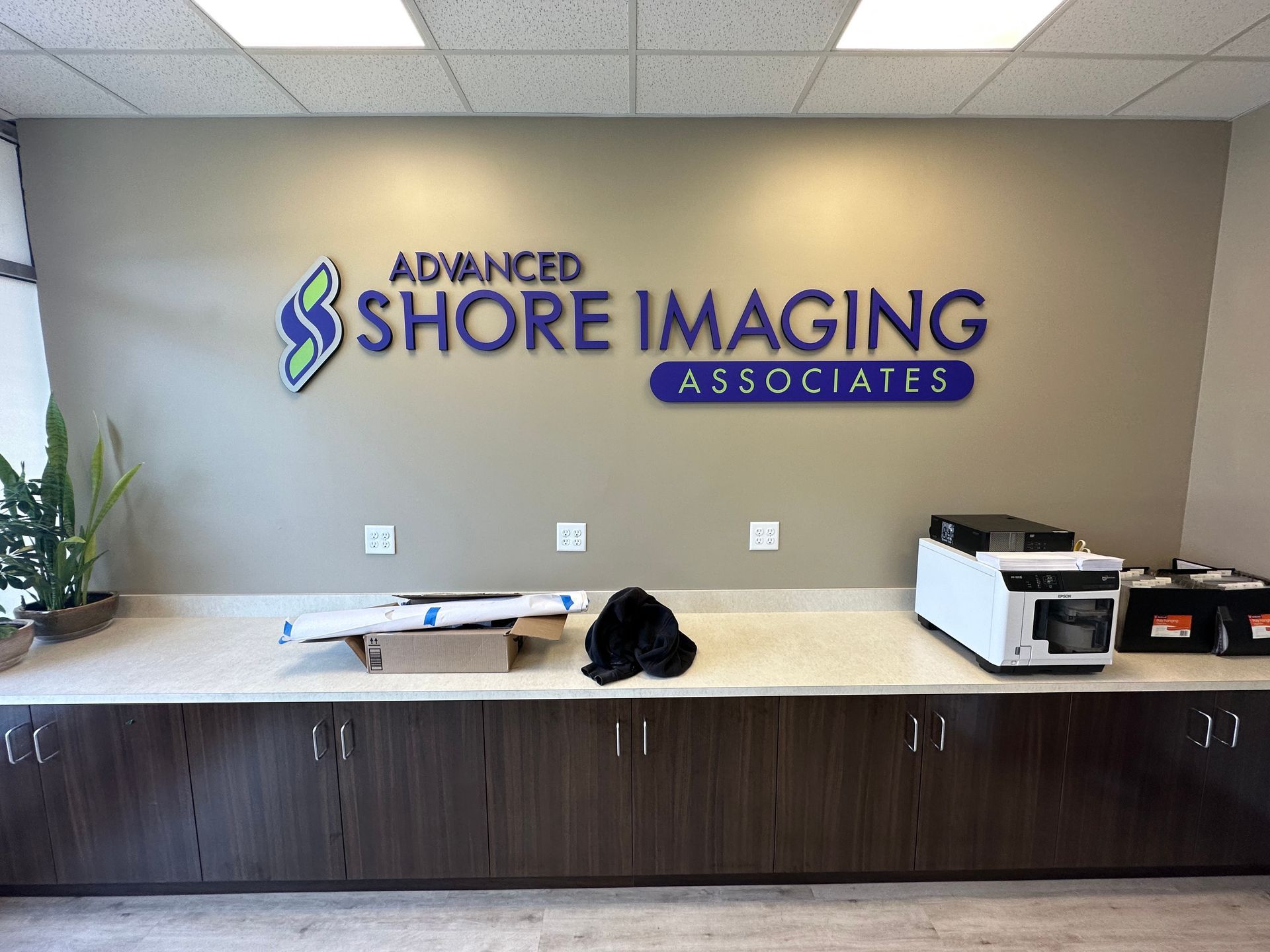 Wall sign for Advanced Shore Imaging Associates, white printer, and supplies on a counter.