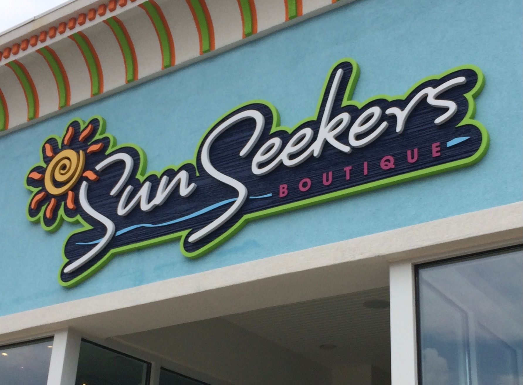 Sun Seekers Boutique sign with a stylized sun, on a light blue building exterior.