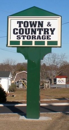 Green sign for Town & Country Storage. White text on a white and brown sign. Outside, sunny day.