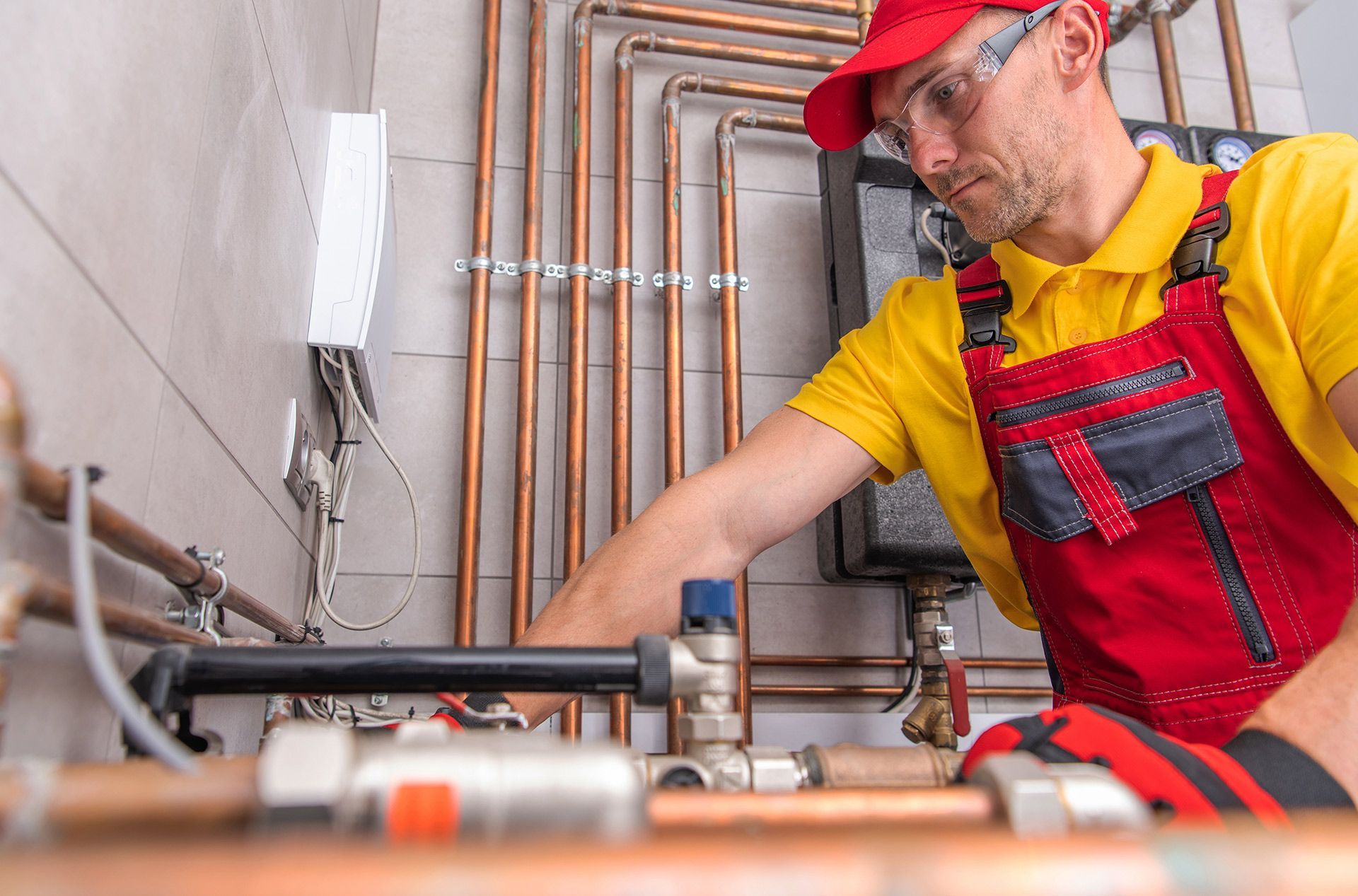Plumber in red overalls and cap repairs copper pipes in a utility room