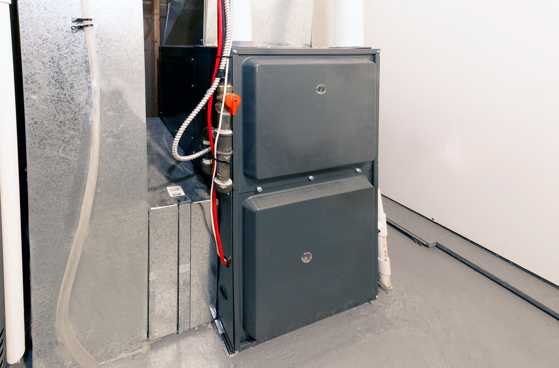 Two stacked dark gray utility boxes with red wiring beside a concrete wall in a utility room