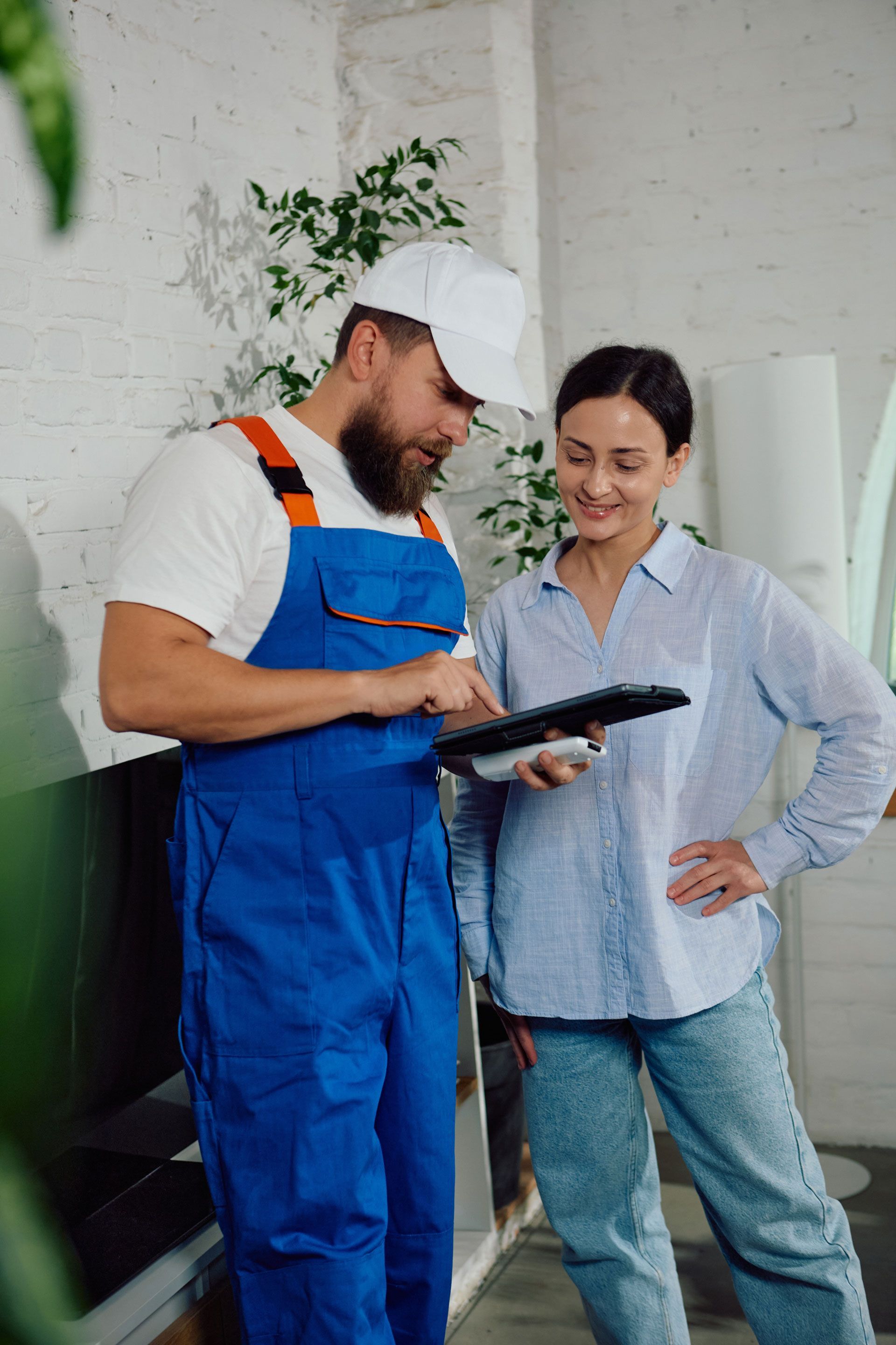 Technician in blue overalls shows a tablet to a woman in a bright workshop