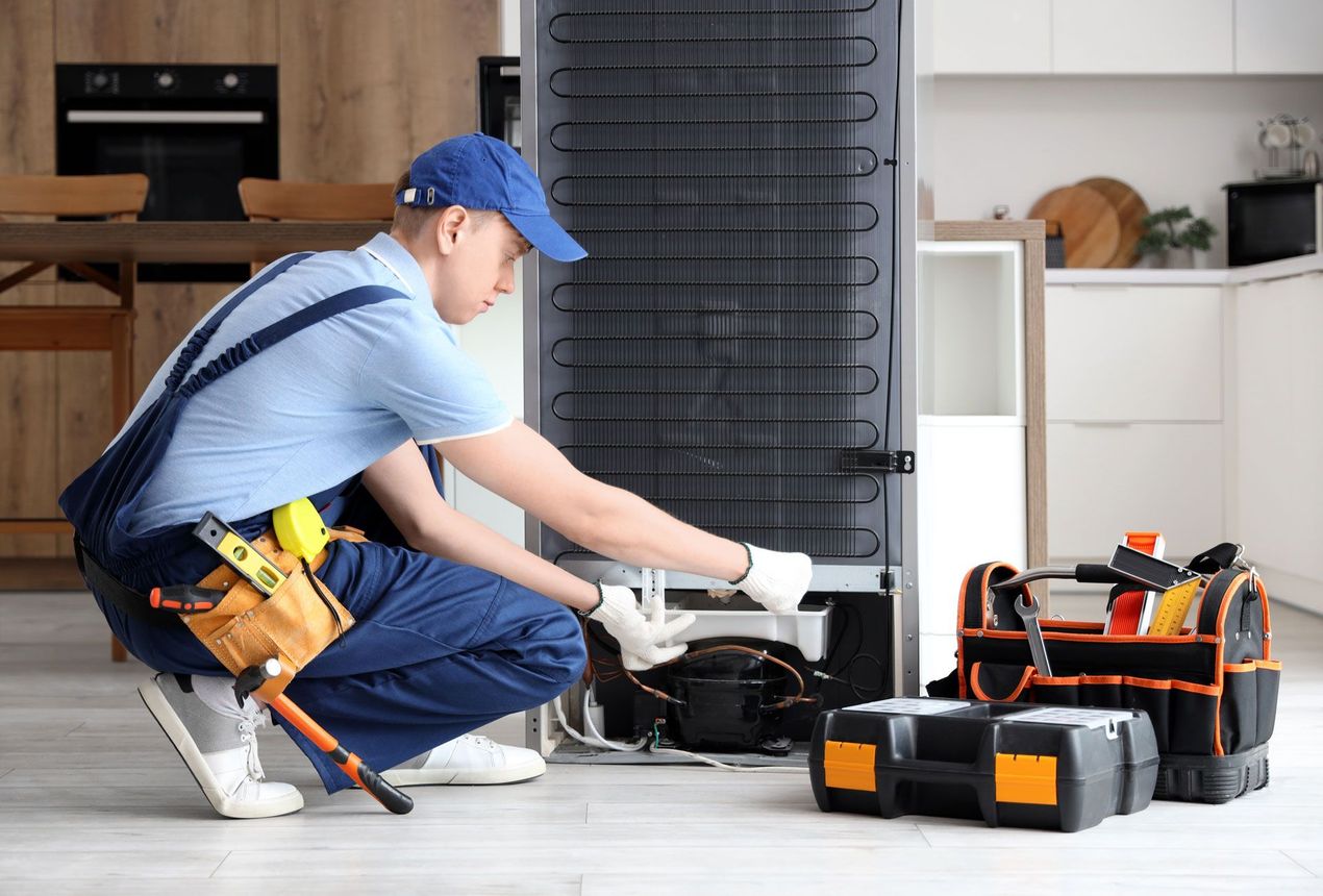 Technician in blue uniform repairing an appliance in a kitchen, with tools and a toolbox nearby