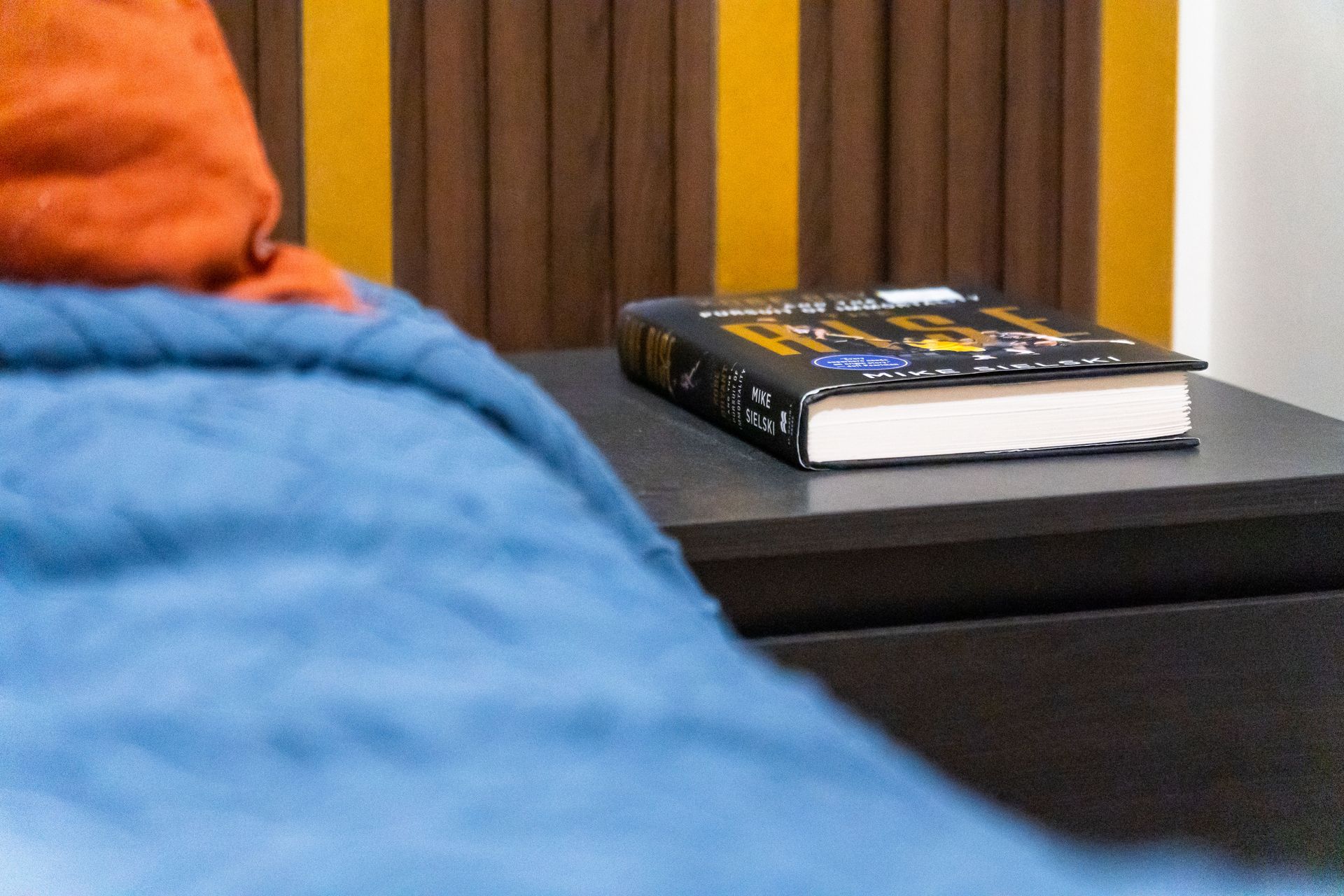 A book is sitting on a nightstand next to a bed.