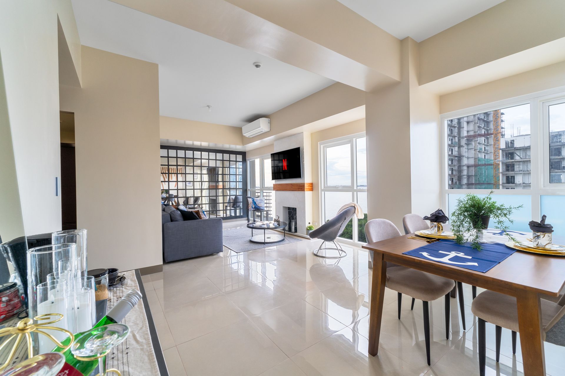 A living room with a dining table and chairs and a large window. Captains Quarters at Bayshore Luxe by Prime, Manila